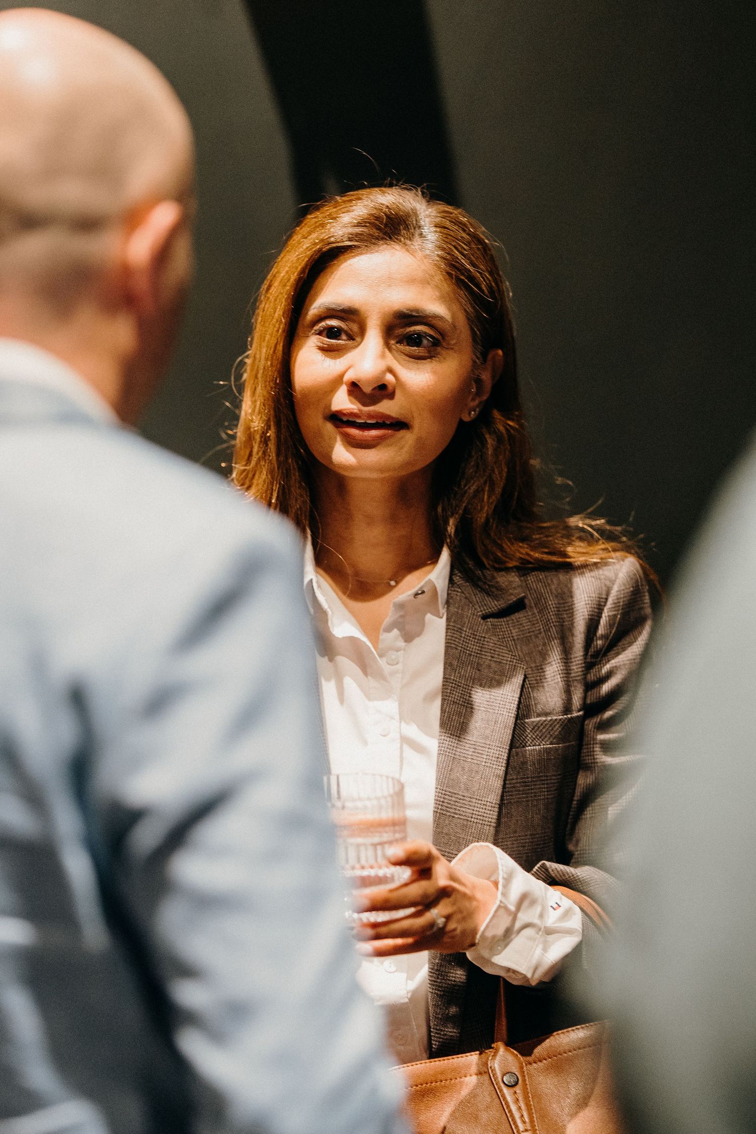 Professional in a grey blazer and white shirt smiles during a business conversation in an office setting.