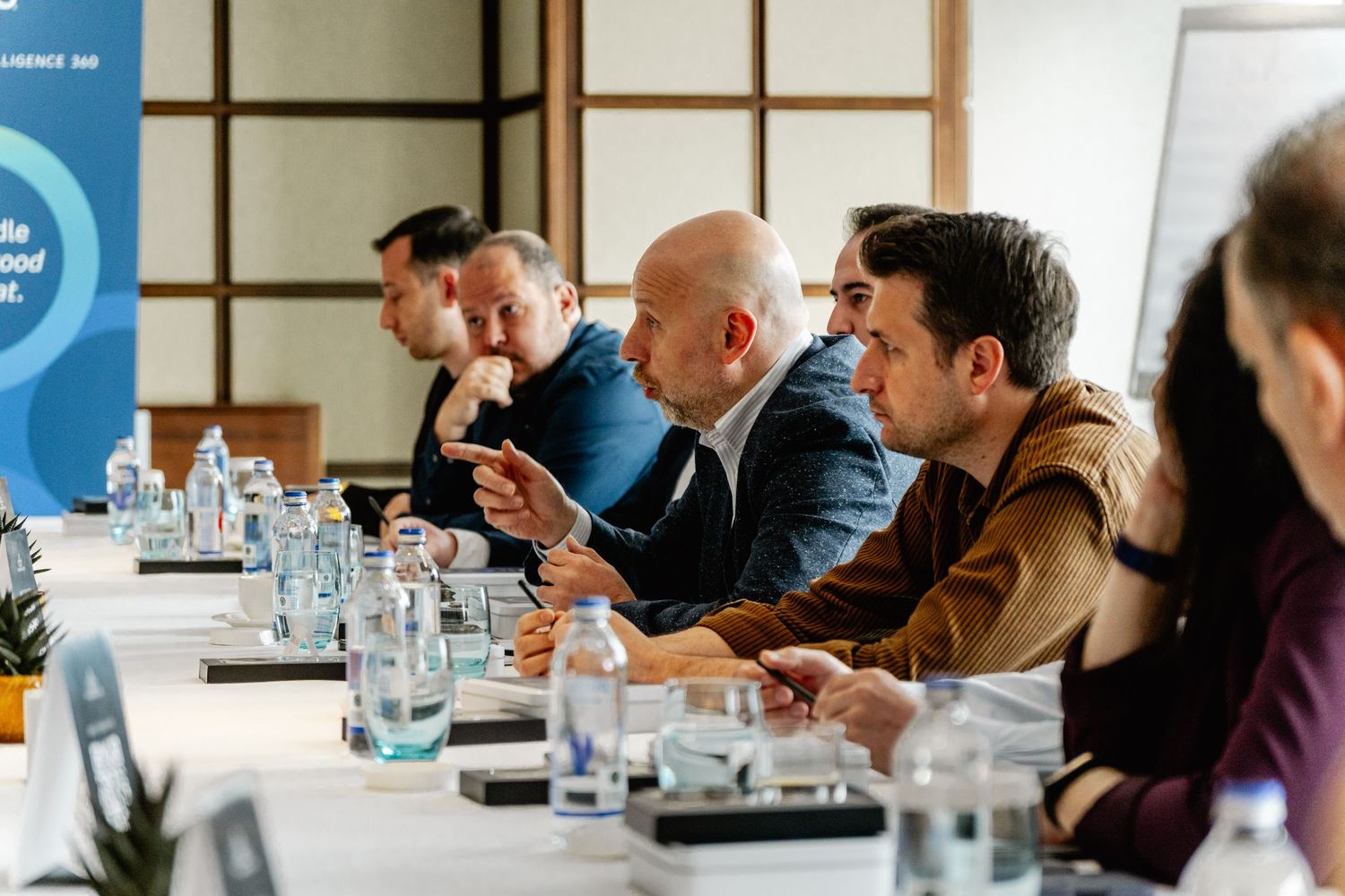 Business professionals engaged in a corporate meeting at a conference table with water bottles and documents.