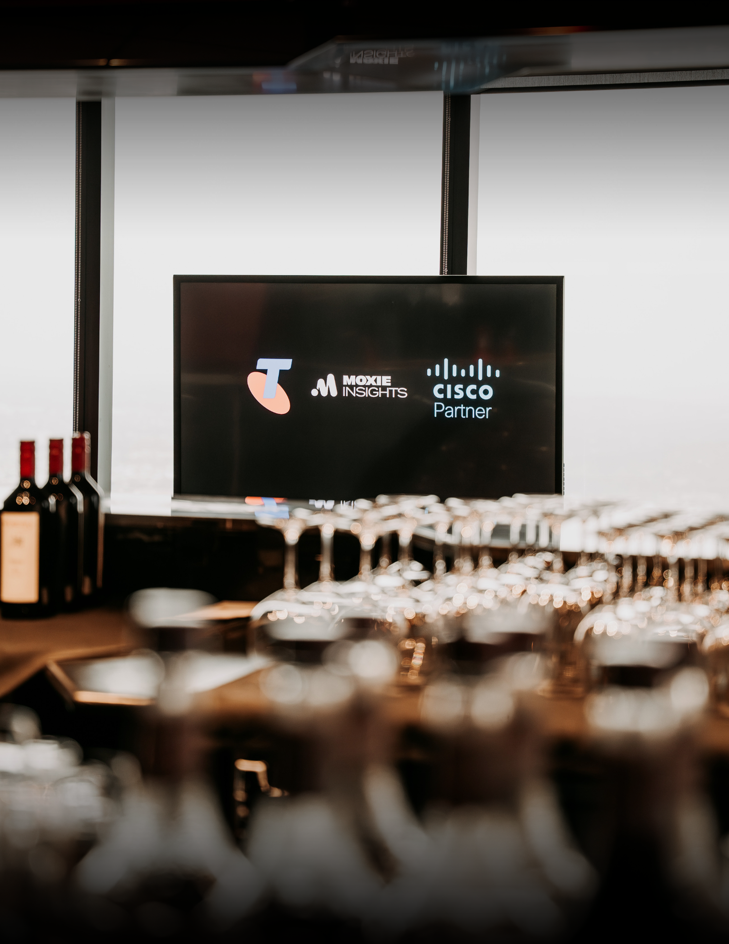 Display screen with Cisco partner logos above table setup with wine bottles and glassware in a dimly lit corporate event space.