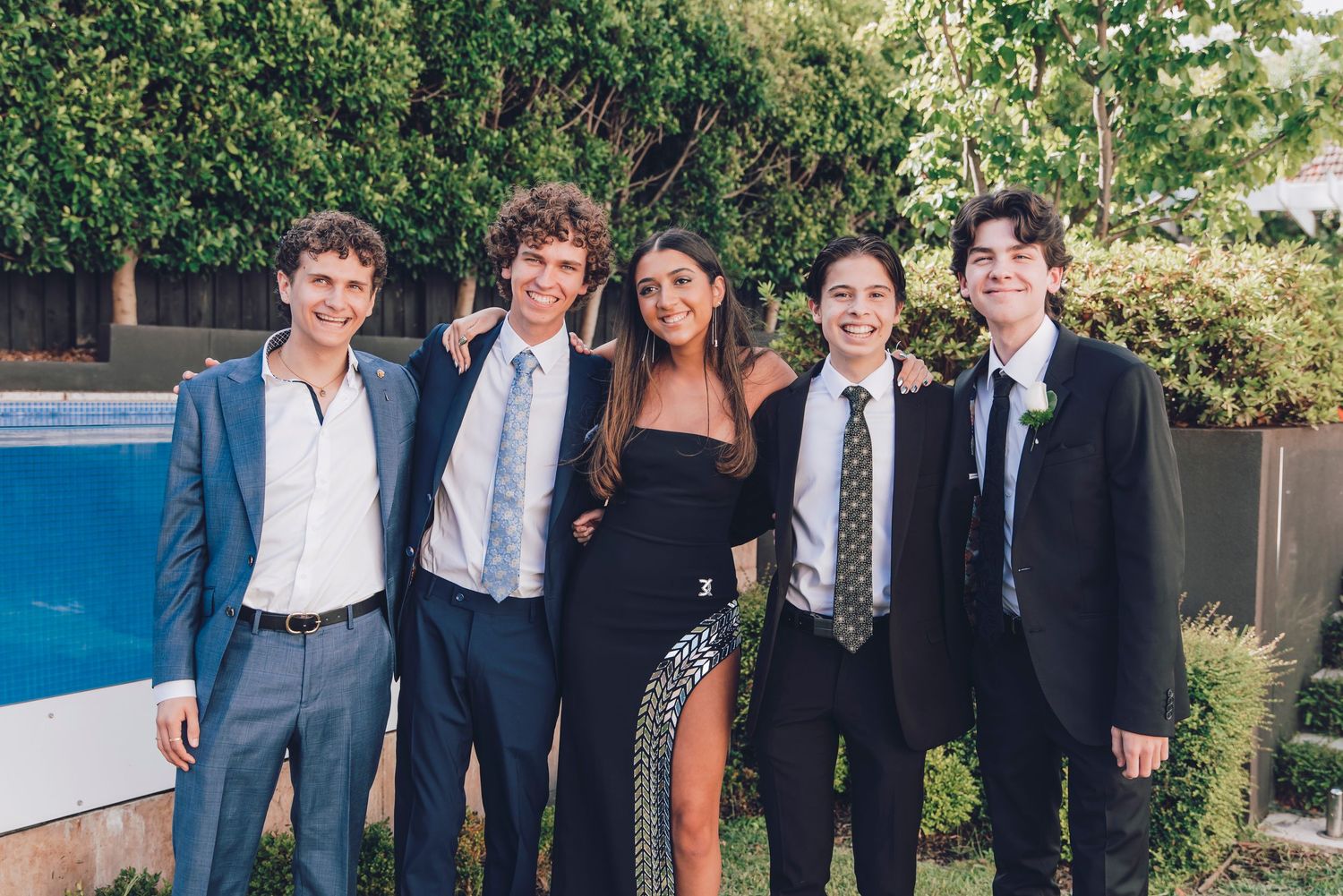 Group of people in formal attire smiling together at an outdoor event during sunset.