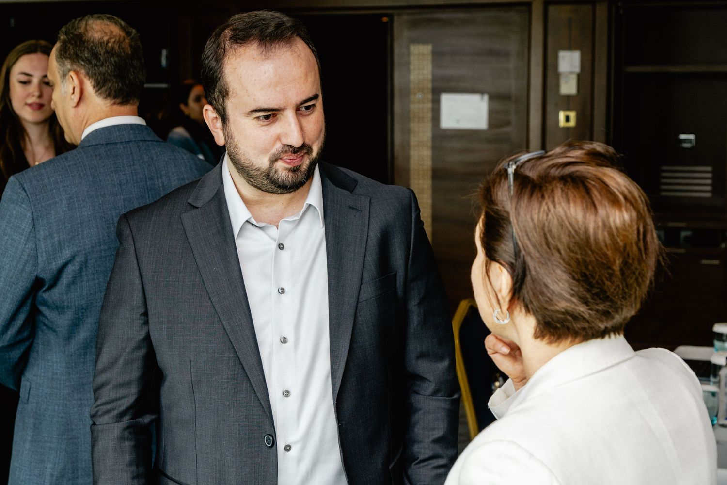 Professional business meeting with man in gray suit conversing with woman in white blazer at corporate event.