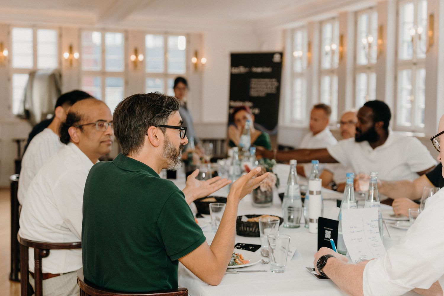 Professionals networking at a formal dinner table in an elegant white dining room during a business lunch event.