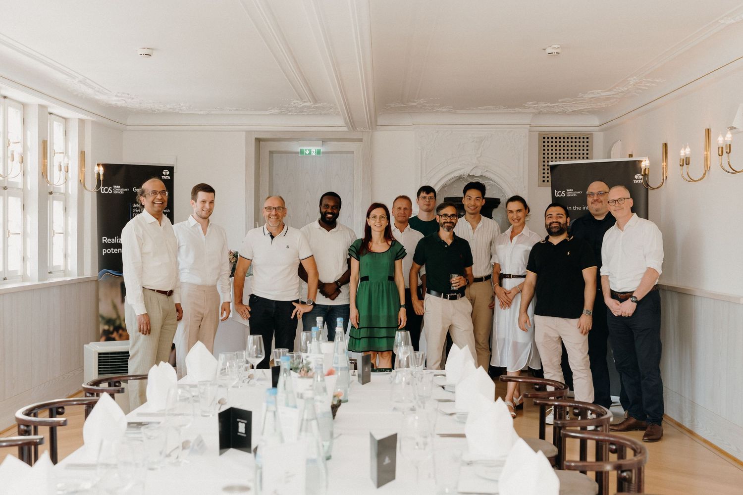 Group of professionals posing together in an elegant white dining room set for a formal event.
