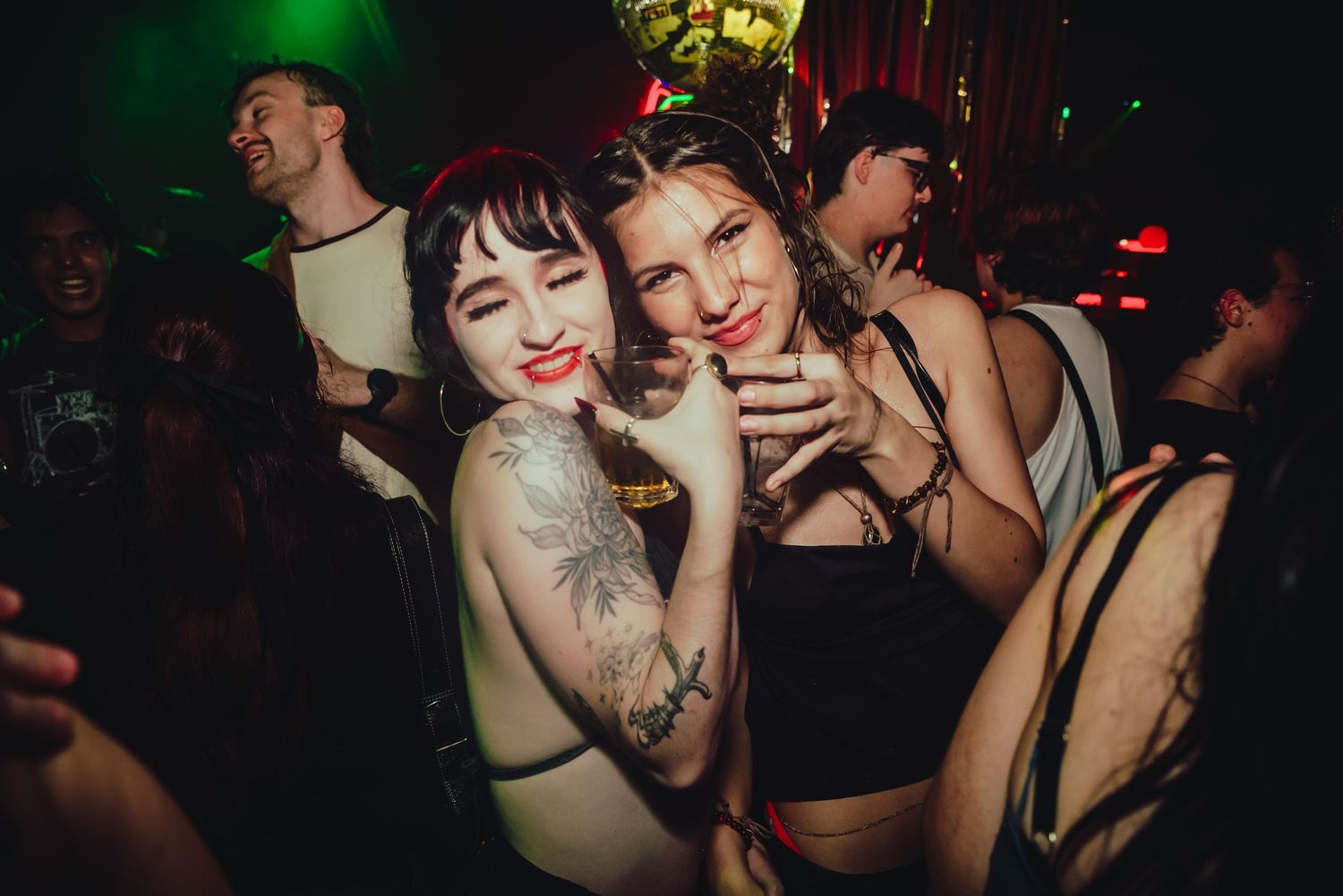 Energetic party scene with people dancing and celebrating under colorful nightclub lighting.