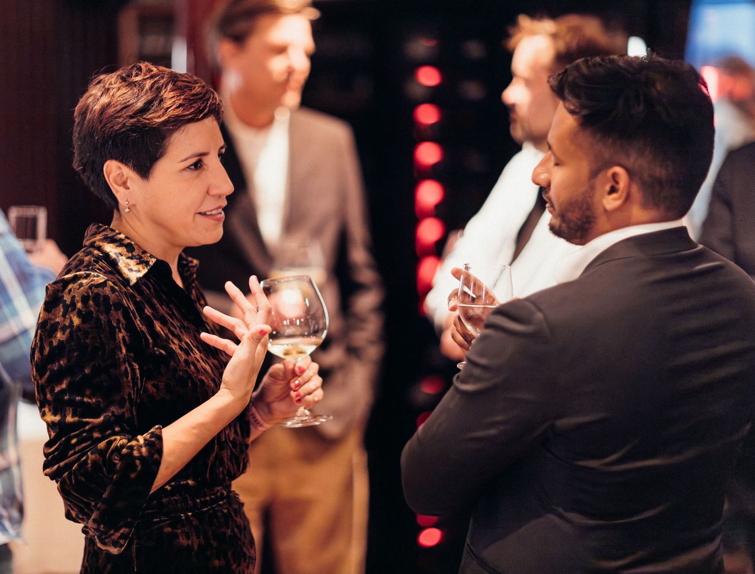 Two people engaged in animated conversation while holding wine glasses at an evening social event.