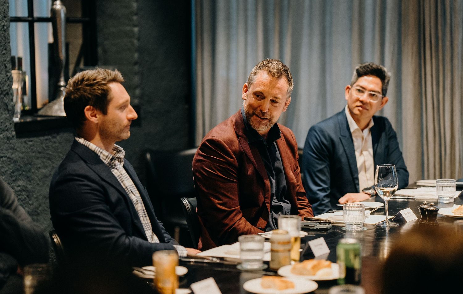 Business professionals engaged in conversation during a meeting at a conference table in a modern office setting.