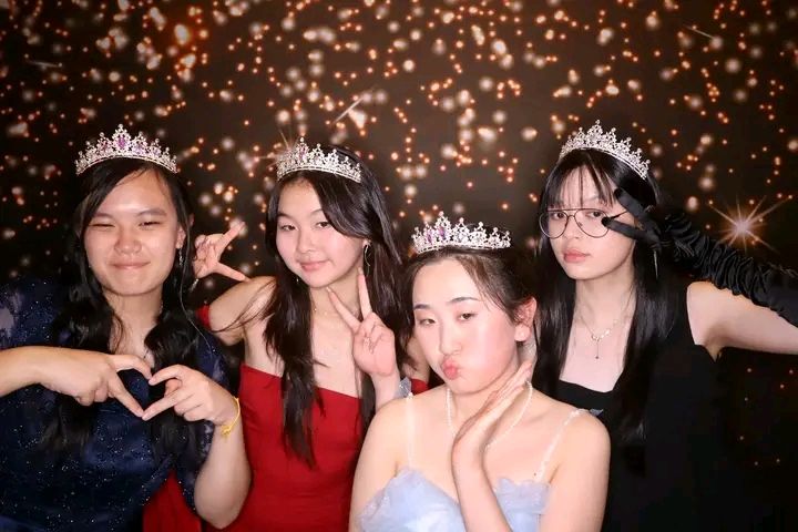 A group of friends poses together at a party with sparkly lights and decorative crowns in the background.