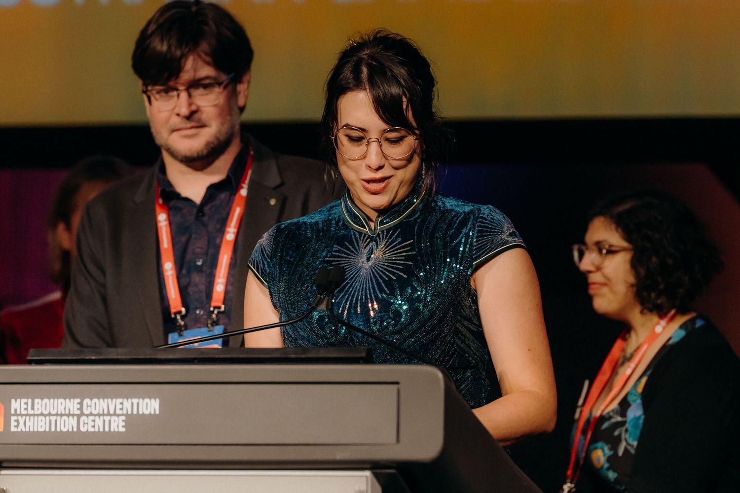 Conference attendees engage in conversation at a dimly lit event with red accents and technical equipment visible.