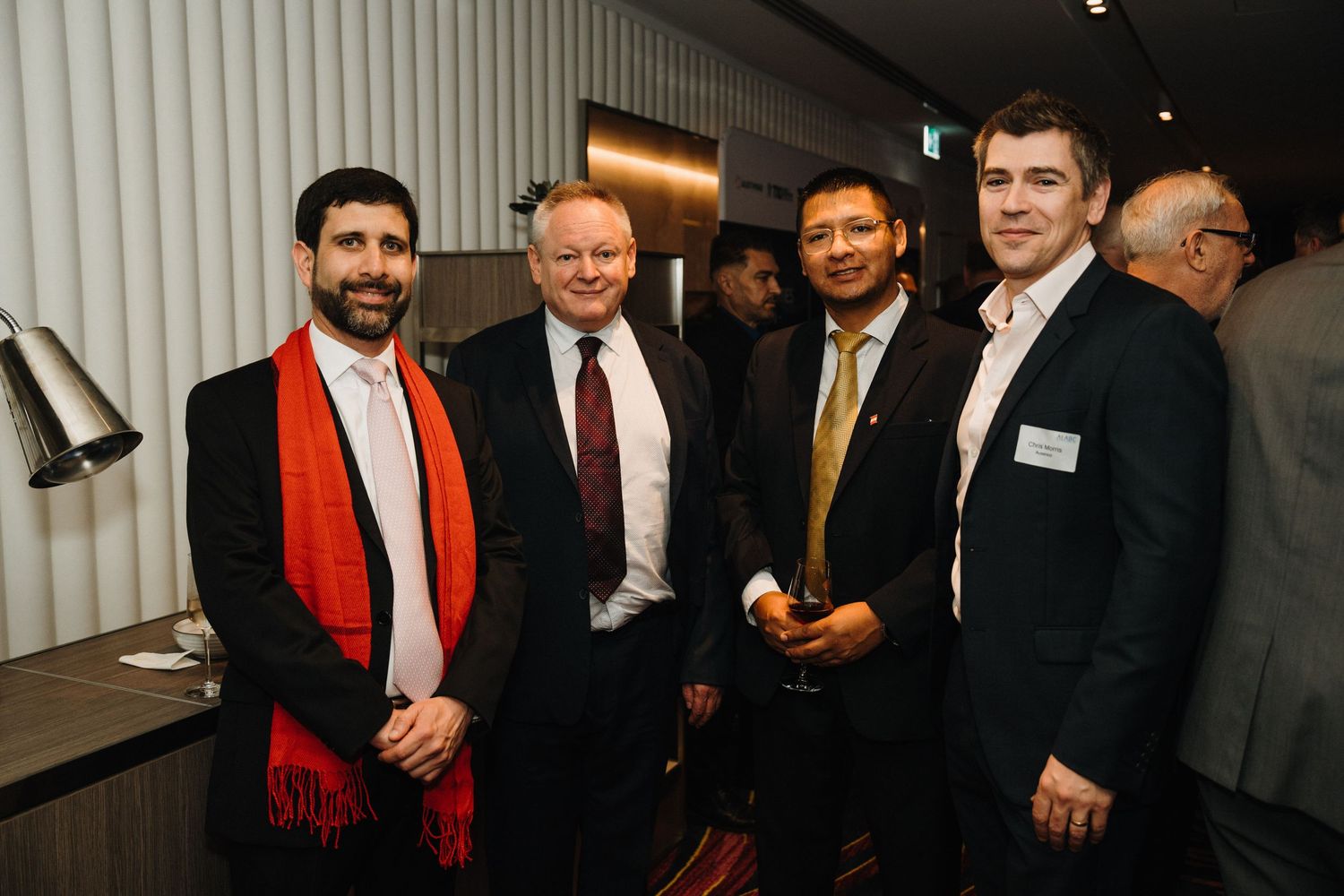 A group of business professionals gather at a networking event in a modern office space.