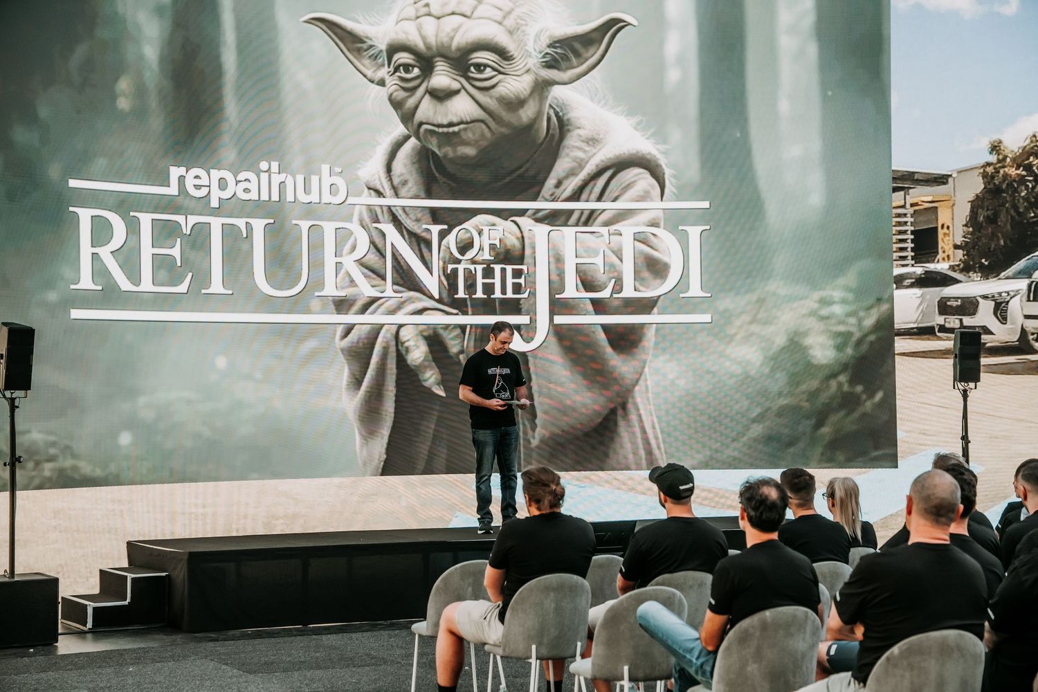 People gather to watch a presentation in front of a large Star Wars Return of the Jedi movie poster featuring Yoda.