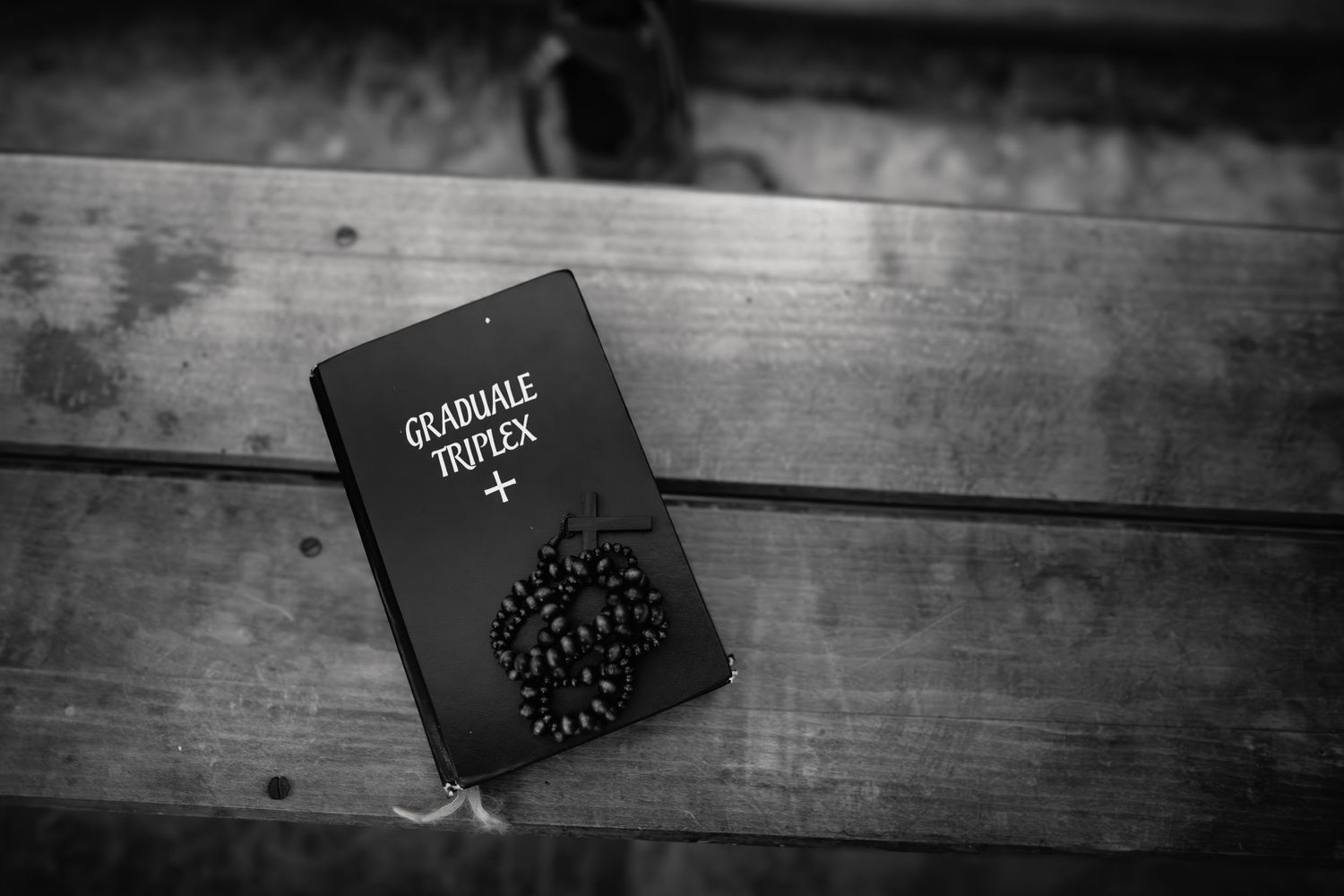 A black graduation cap with tassel rests on a wooden surface viewed in black and white.