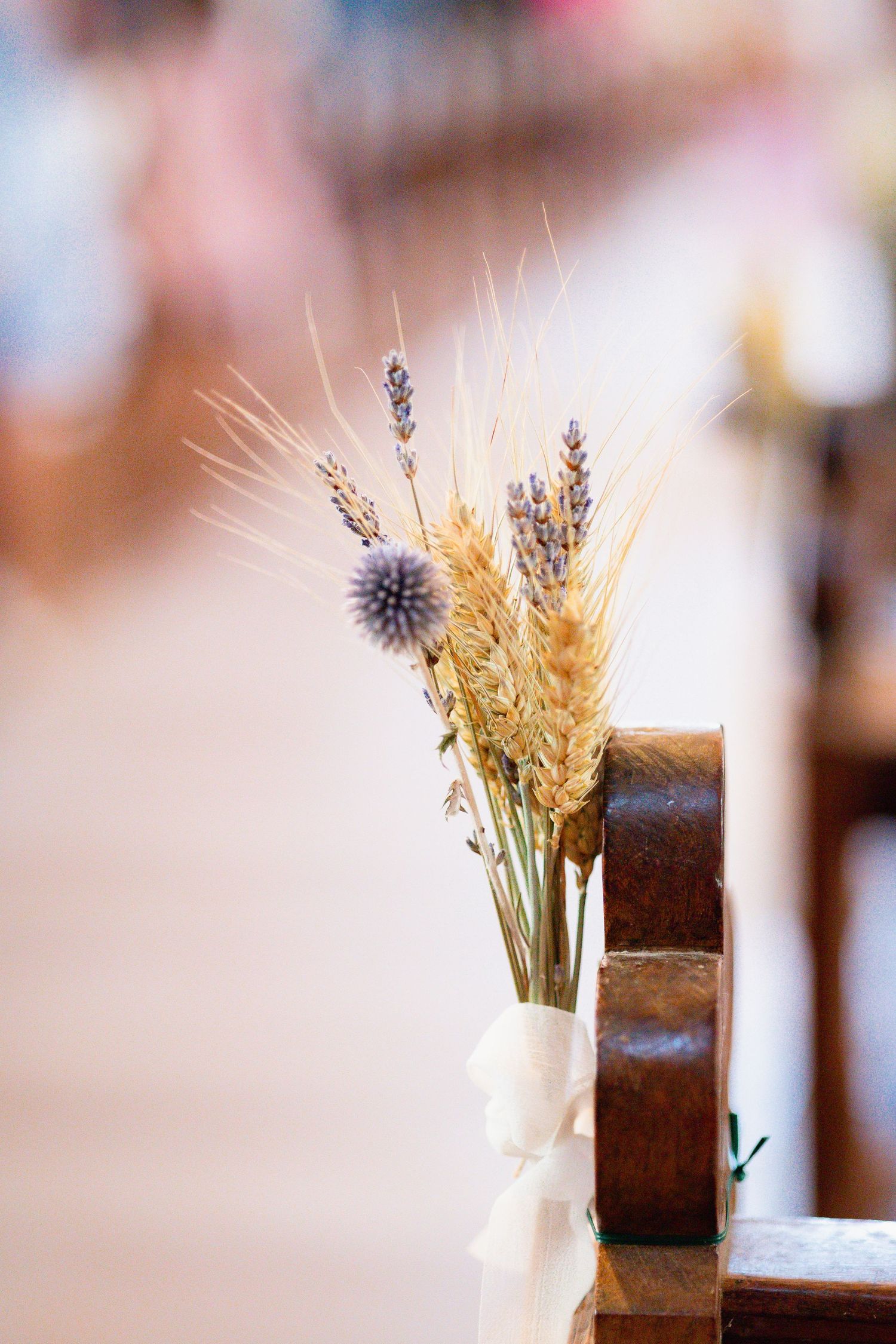 Rustic wedding decoration with dried wheat stalks, lavender sprigs and thistle tied with white ribbon on wooden chair.