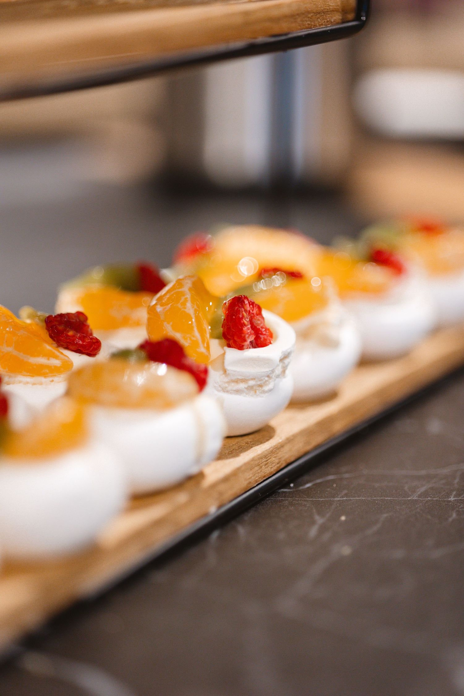 Mini desserts lined up on a wooden board garnished with orange slices and berries.