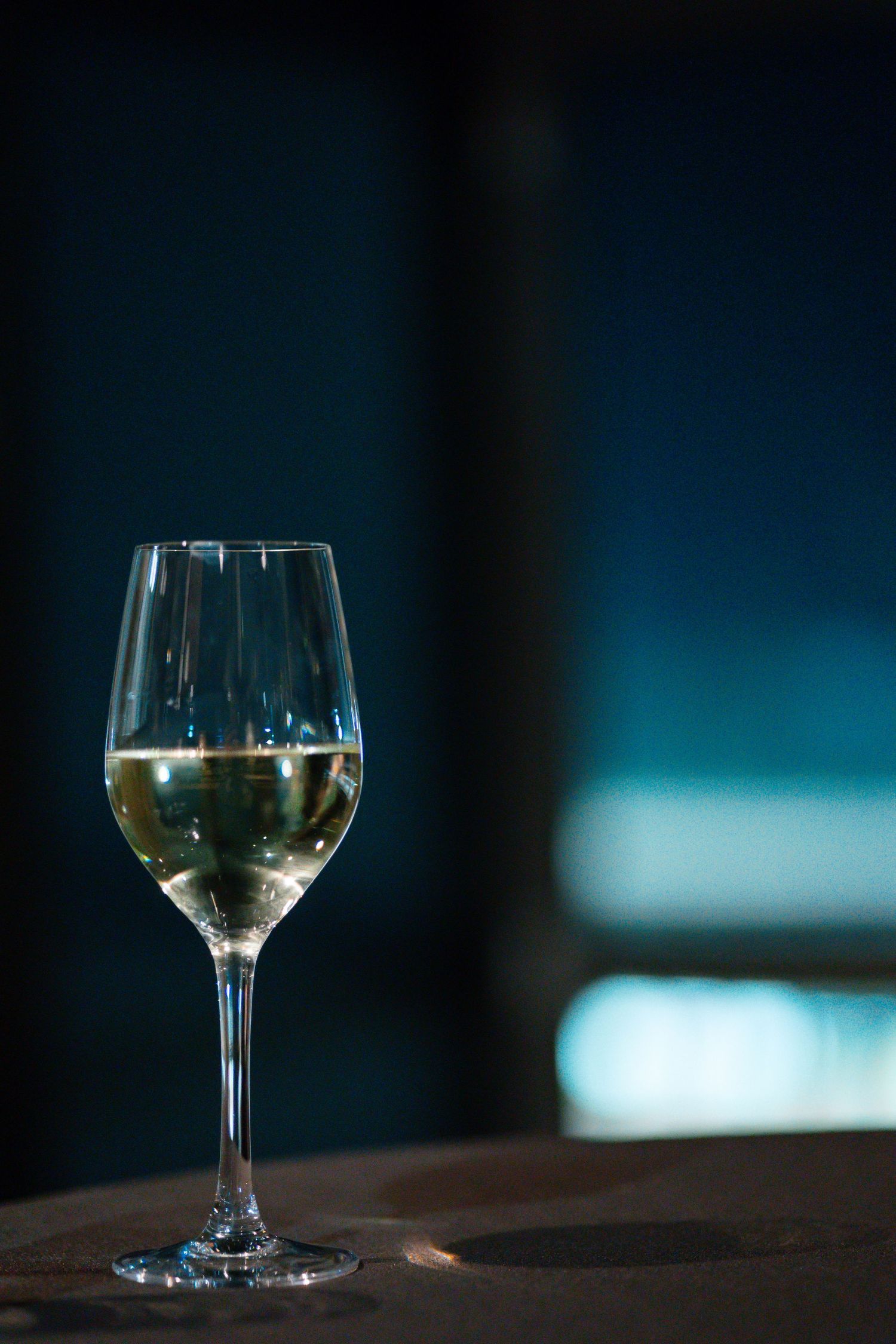 Glass of white wine photographed against dark blue background.