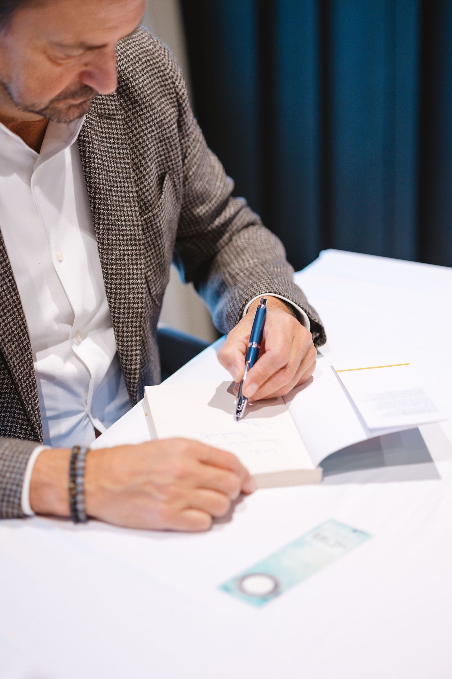Person in tweed jacket signing books at white table during event.