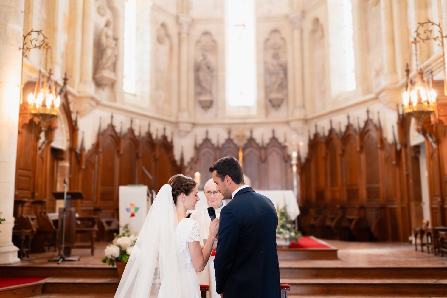 Bride and groom share intimate moments during wedding ceremony inside ornate church with gothic architecture and chandeliers.
