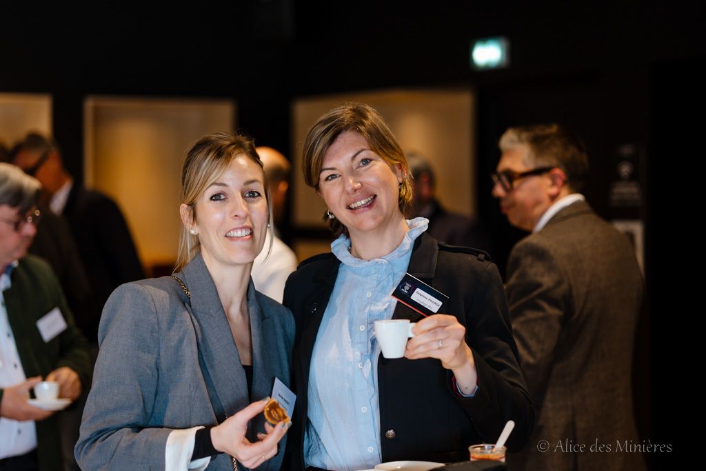 Two professionals in business attire networking at an indoor corporate event while enjoying refreshments.