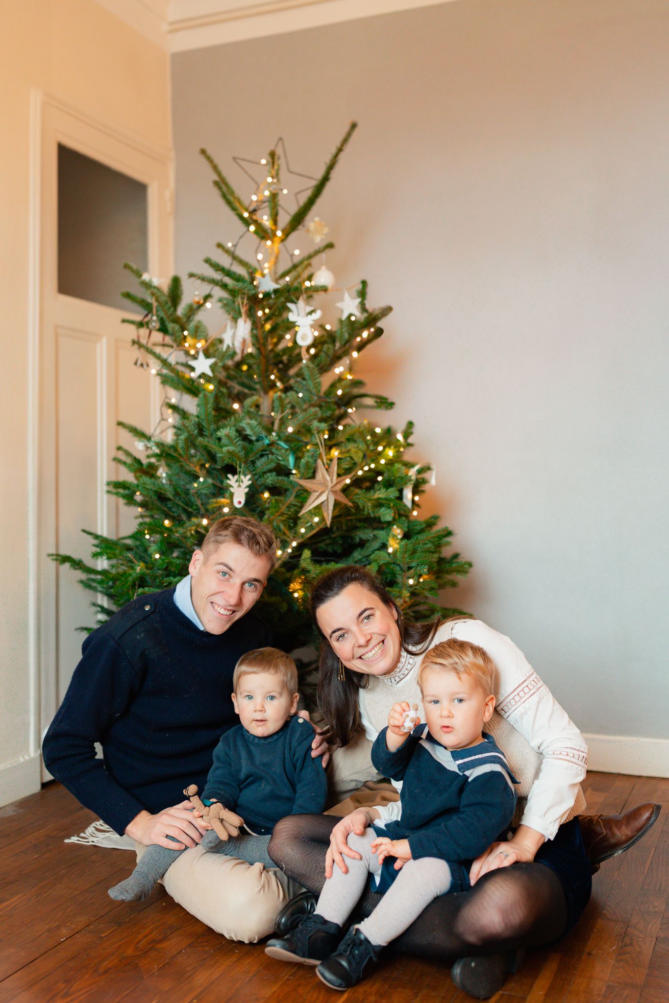 Photo de famille devant le sapin Noël, photo enfants et parents avec de larges sourires.