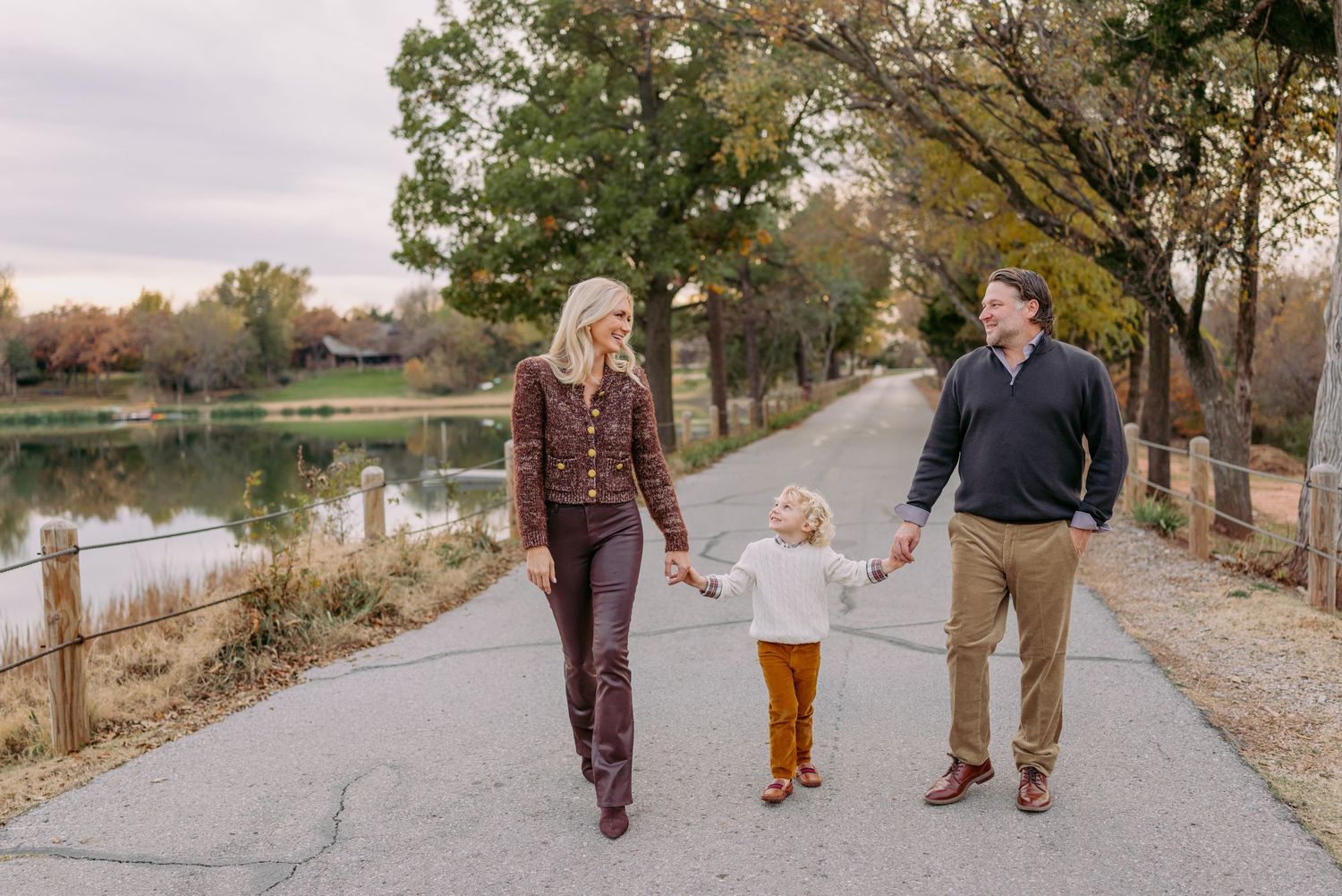 A family walks together on a tree-lined path during autumn with colorful fall foliage in the background.