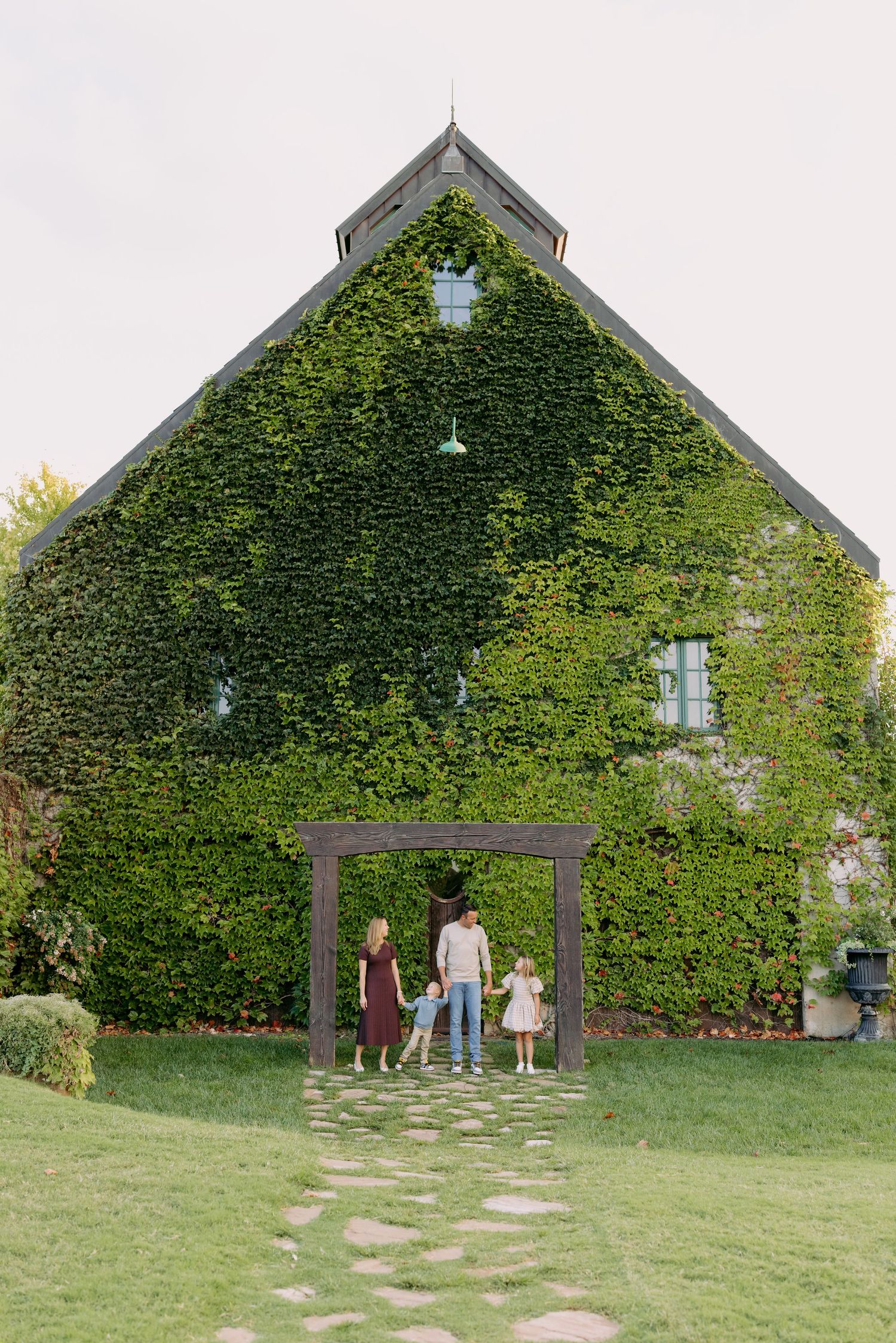 Three barn-style buildings covered in lush green ivy with stepping stones leading to their entrances.