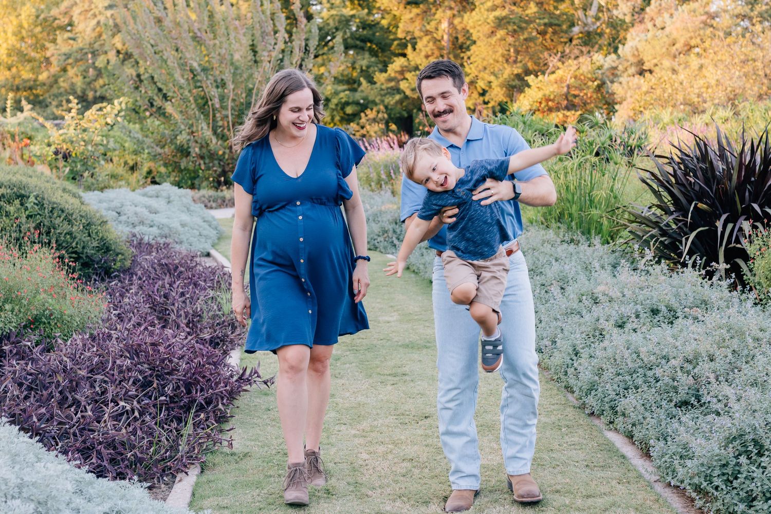 A family takes a stroll together through a beautiful garden path lined with purple lavender and autumn foliage.
