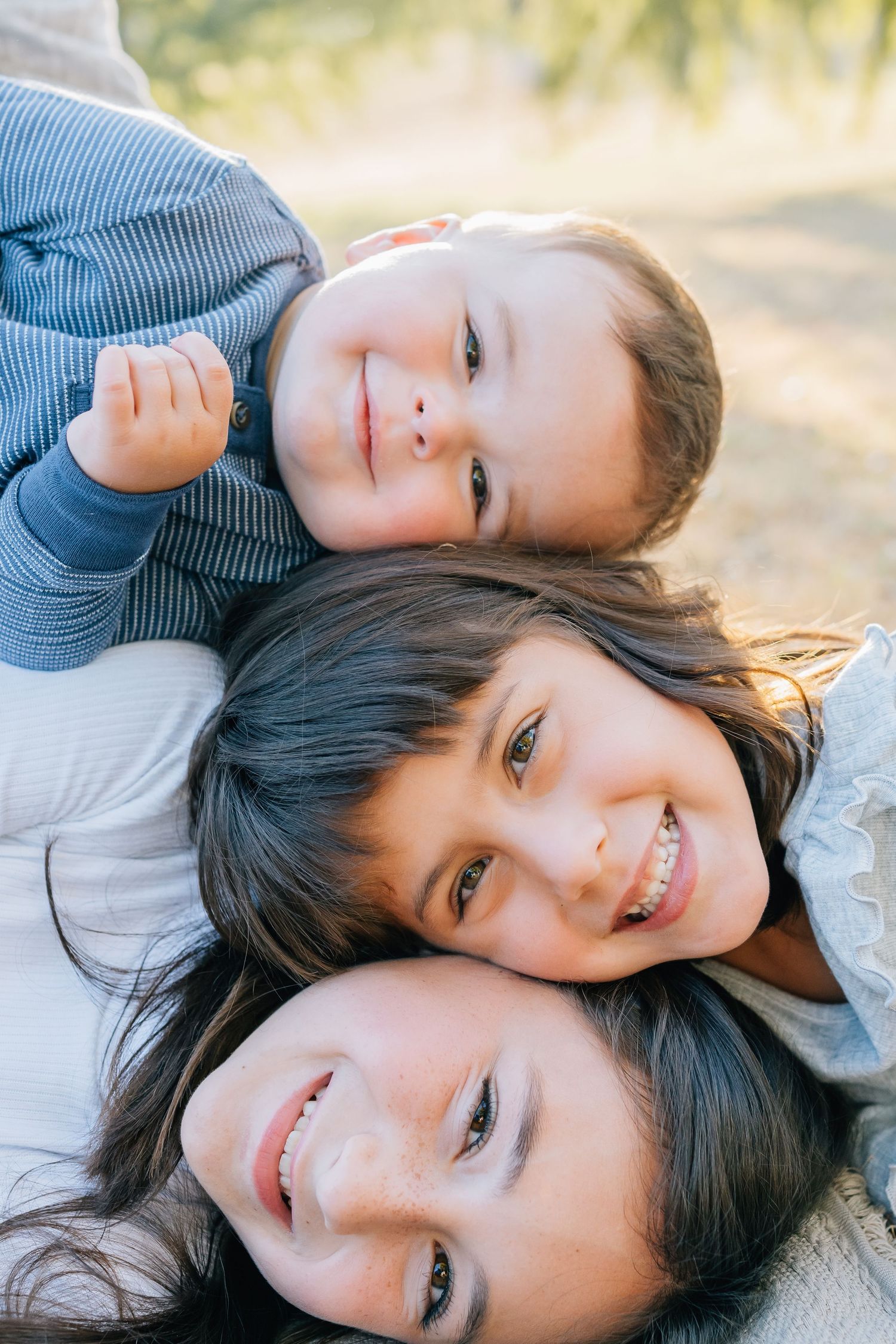 Three people lying down together in a close portrait outdoors.