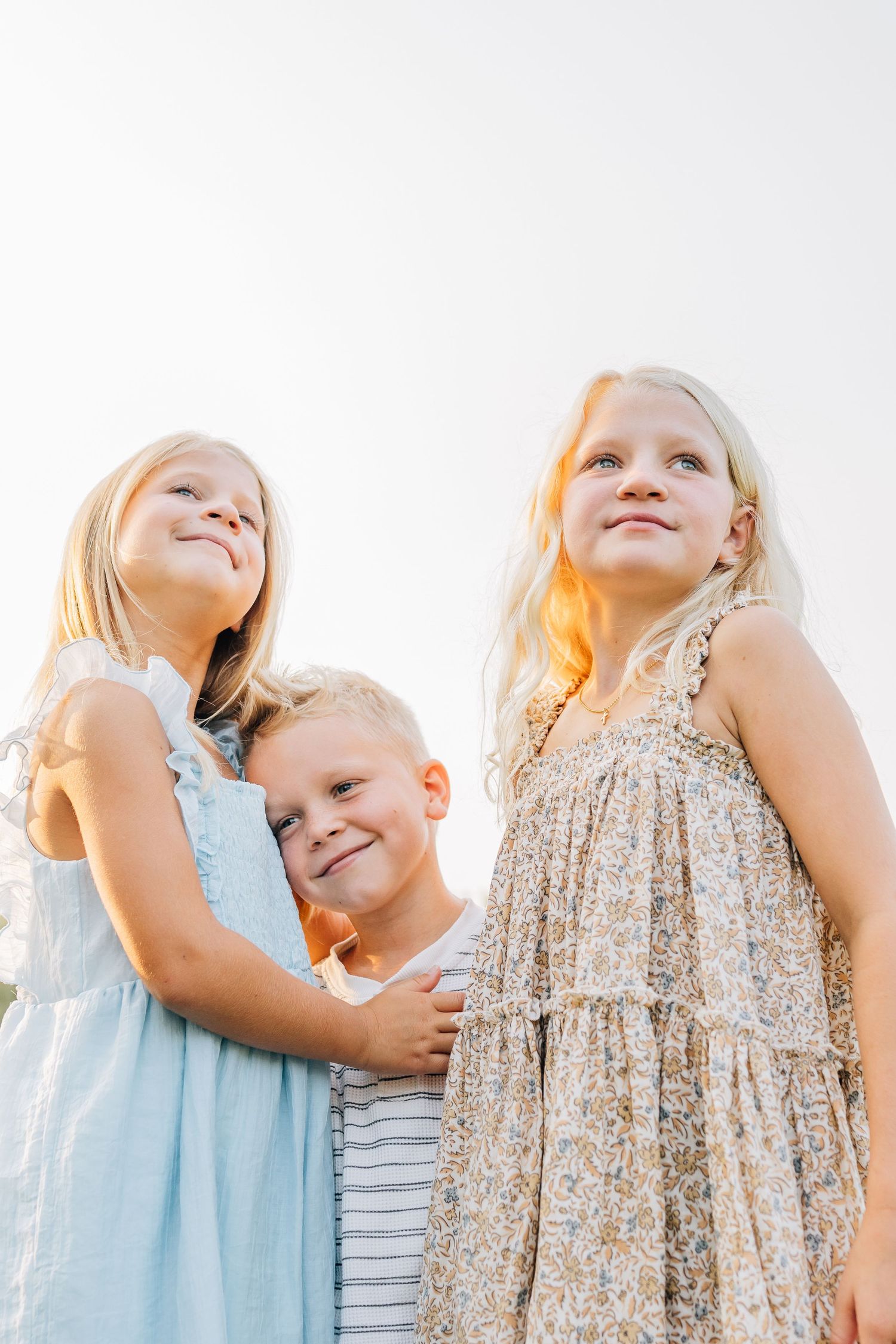 Three children standing together looking up with sunny golden lighting.