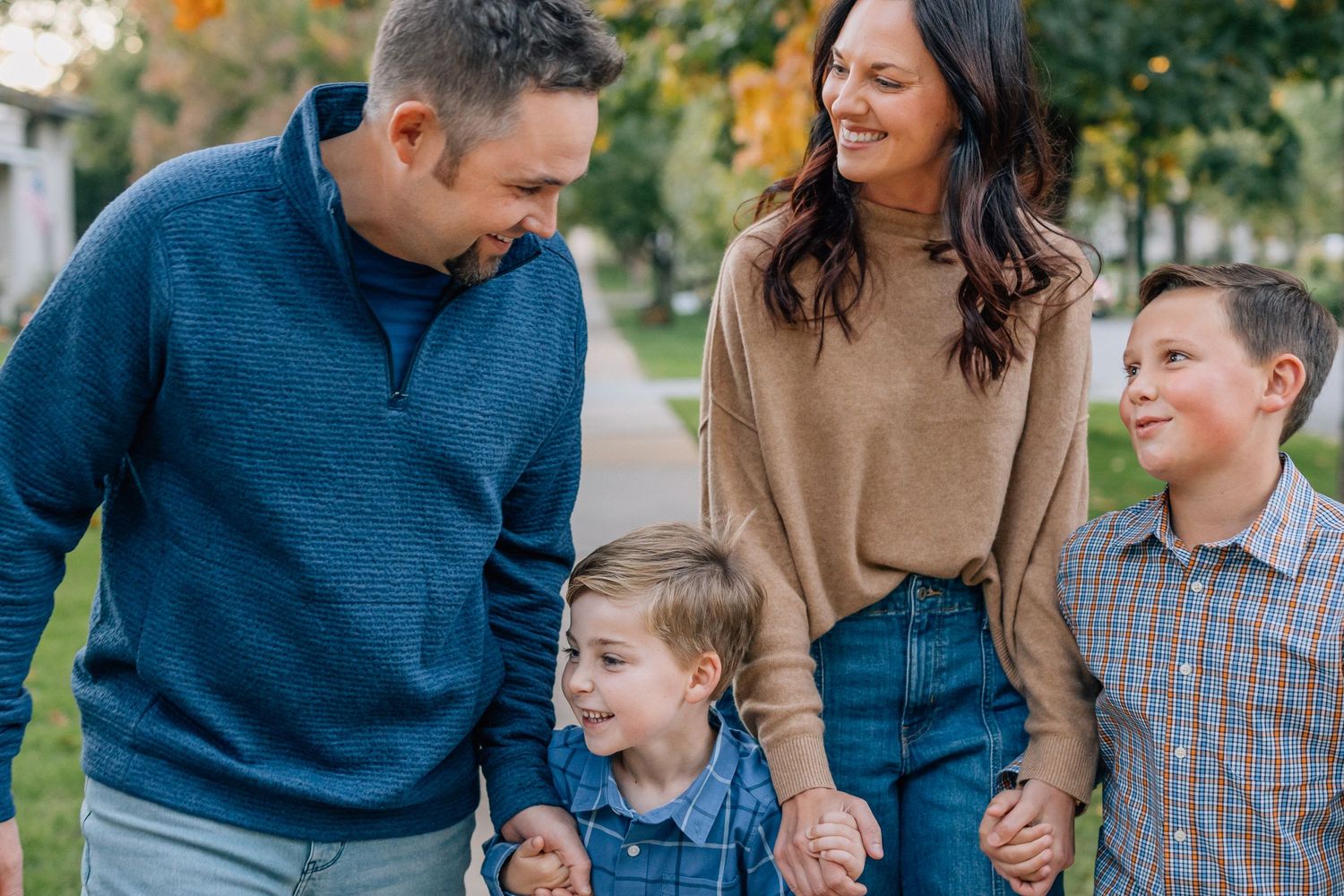 A joyful family walks together outdoors on an autumn day wearing casual sweaters and denim.