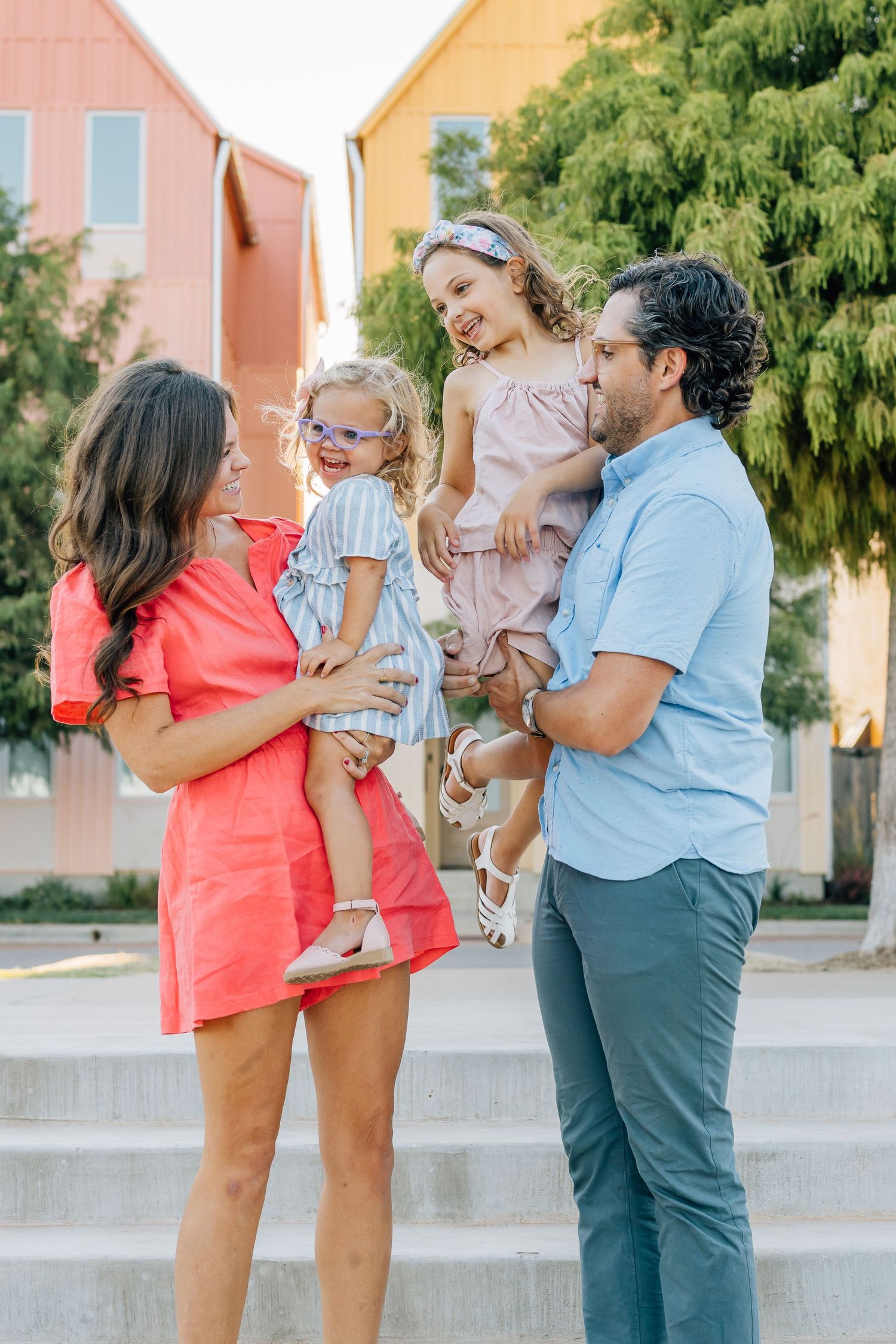Family gathered on outdoor steps near pink and yellow buildings.