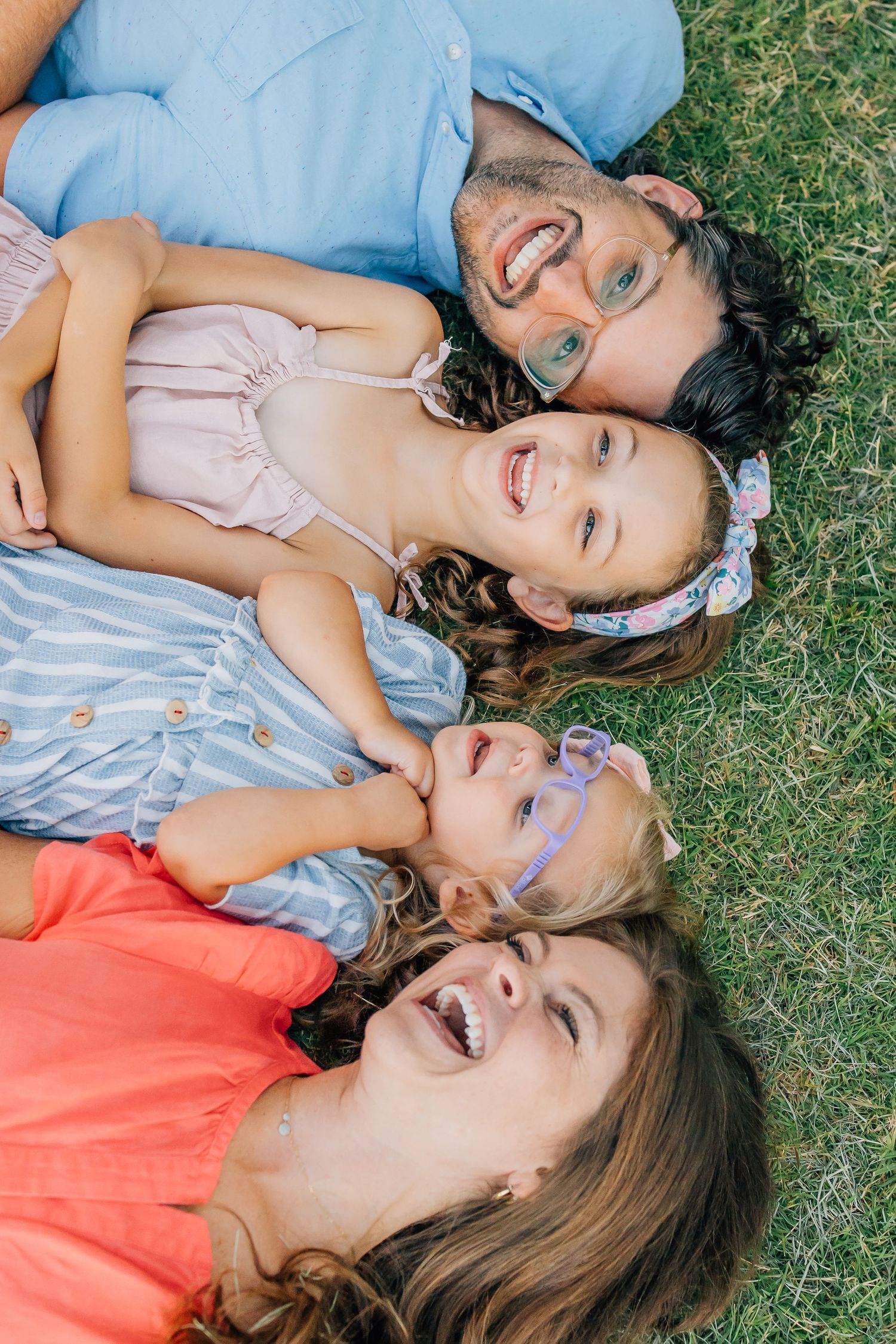 Family lying on grass together laughing and smiling at the camera.