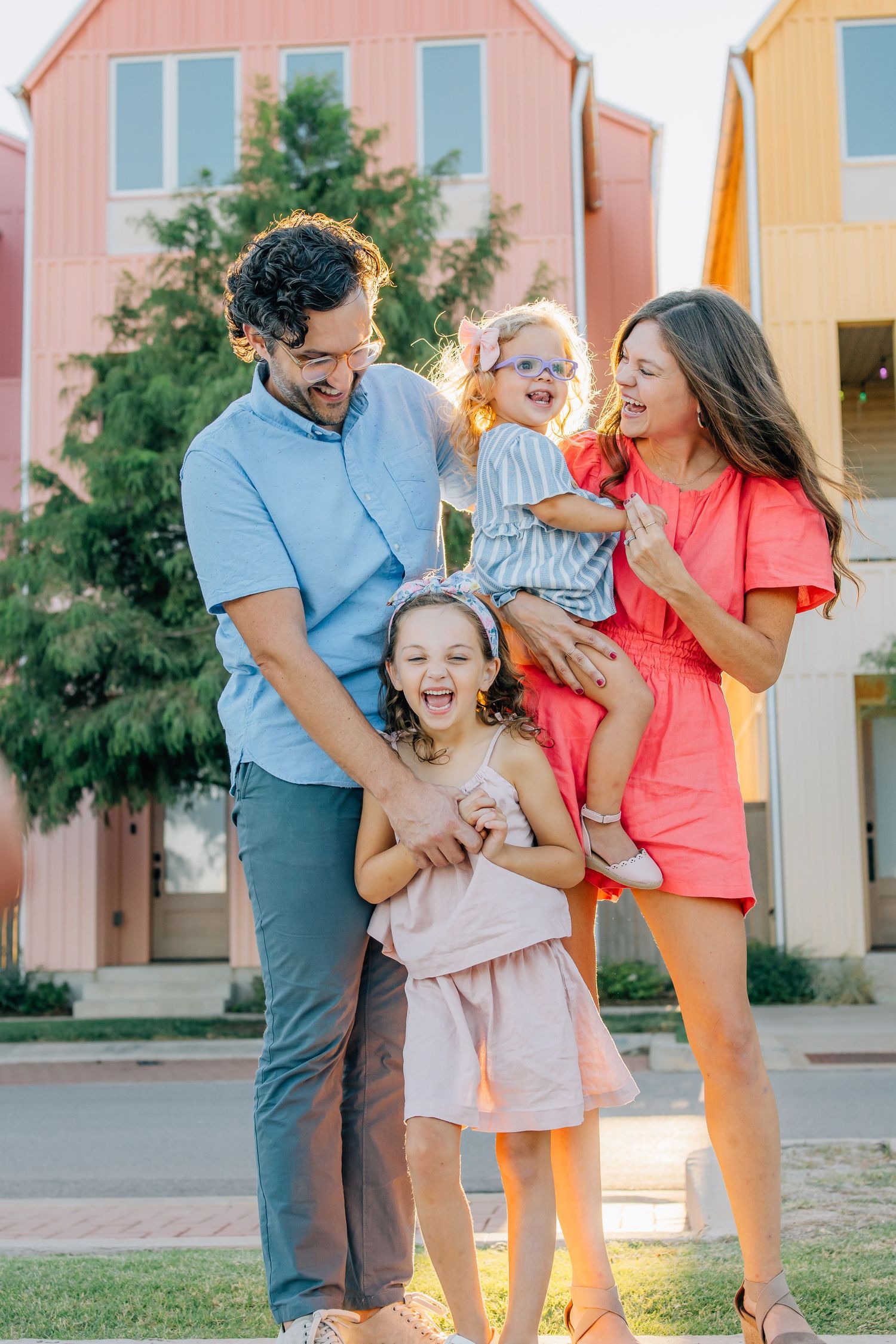 A joyful family moment captured outdoors in front of colorful pastel townhouses during golden hour.