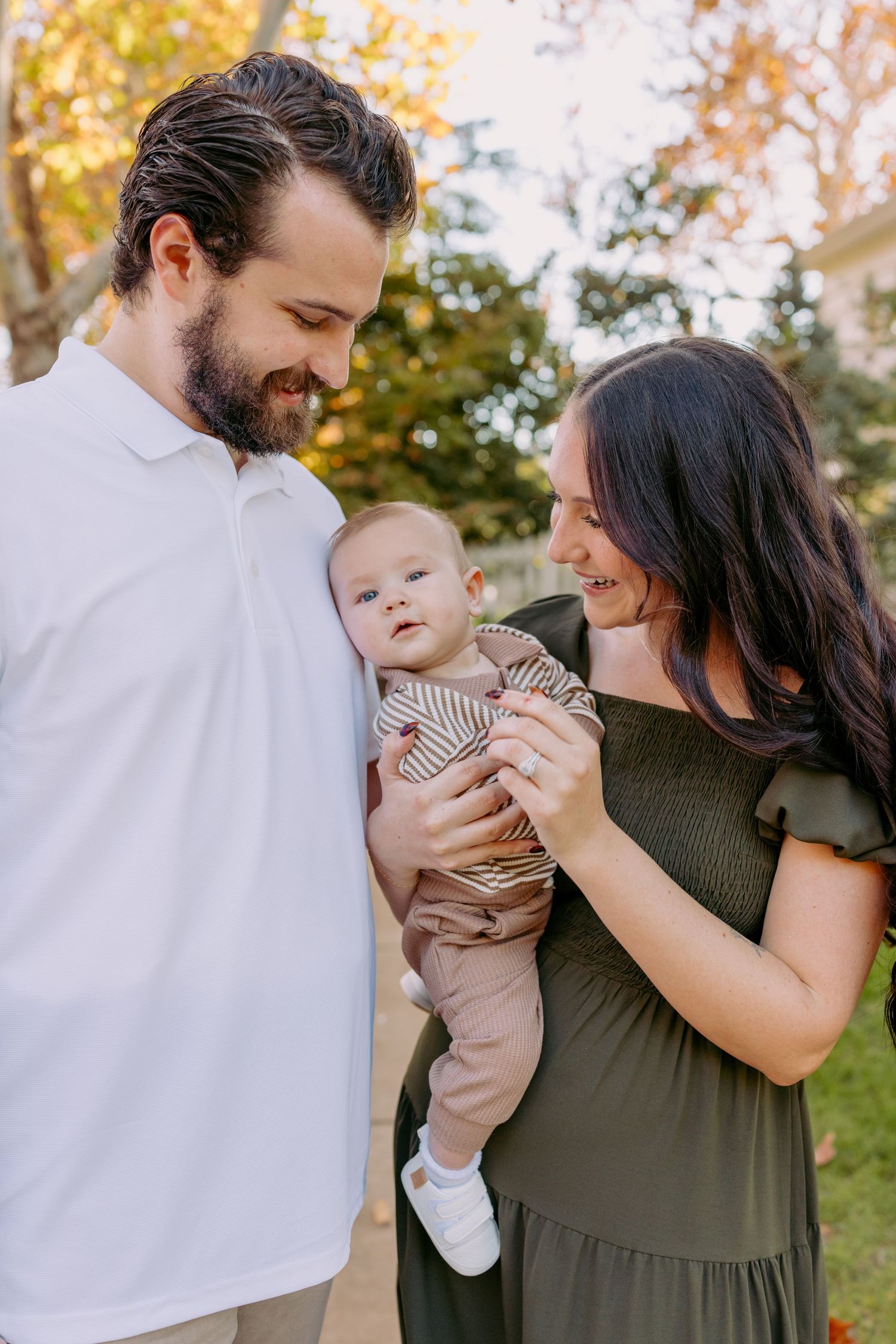 A family shares tender moments together in an outdoor setting during autumn with golden foliage in the background.