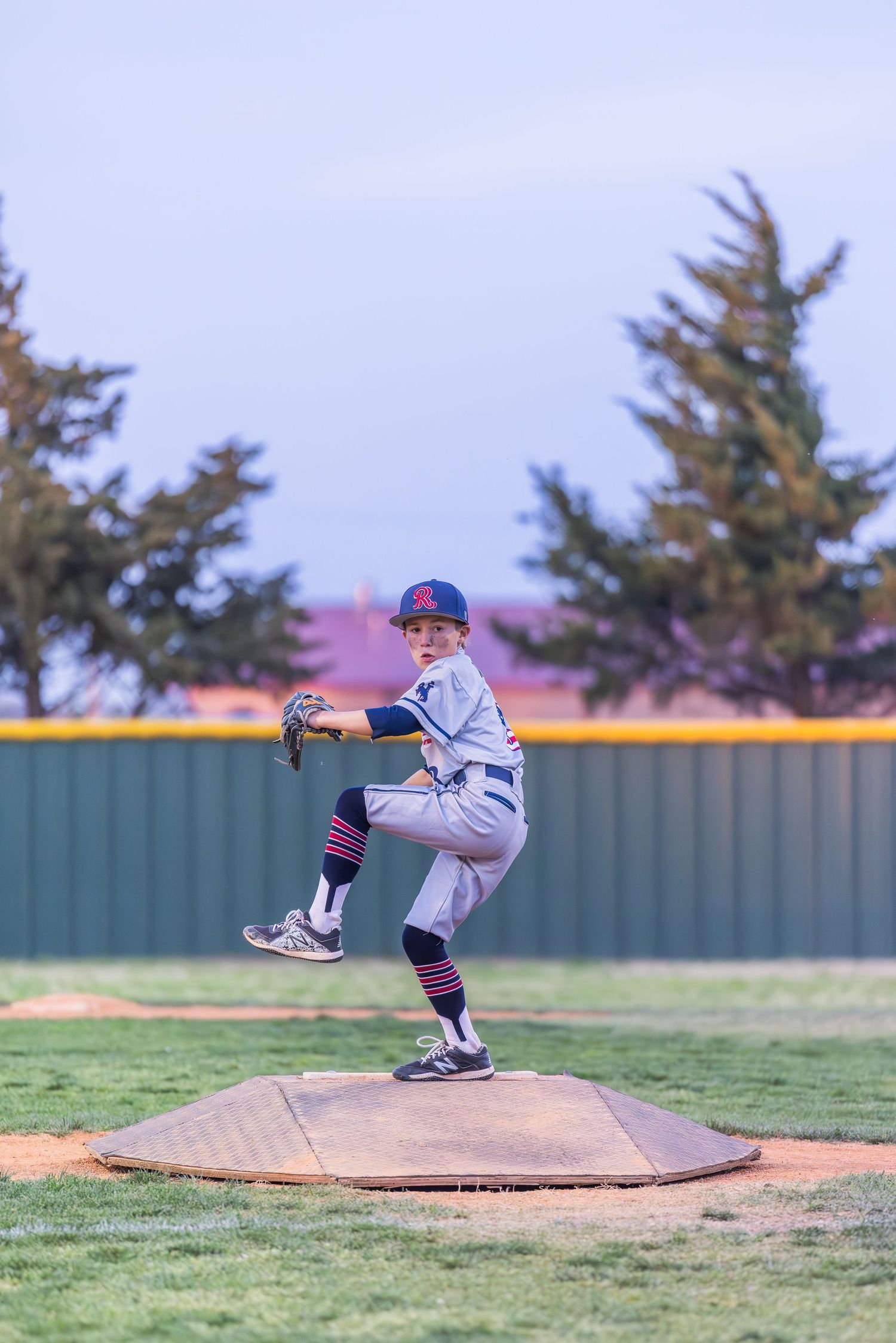 Baseball pitcher in gray uniform stands on pitcher's mound in wind-up position during game at baseball field.