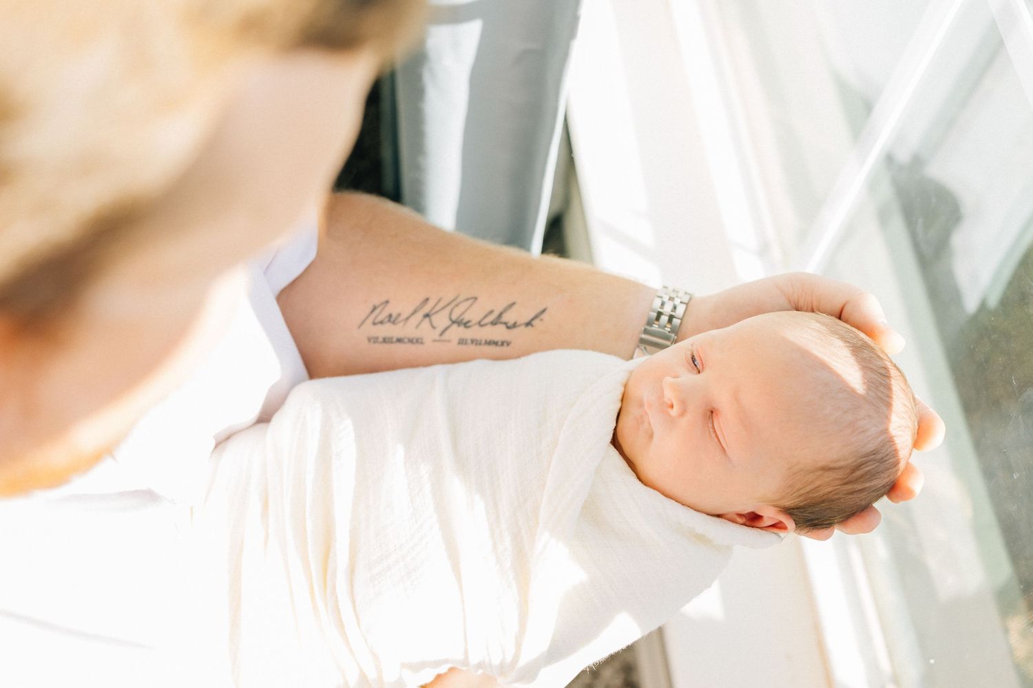 Gentle hands holding sleeping newborn wrapped in white blanket.