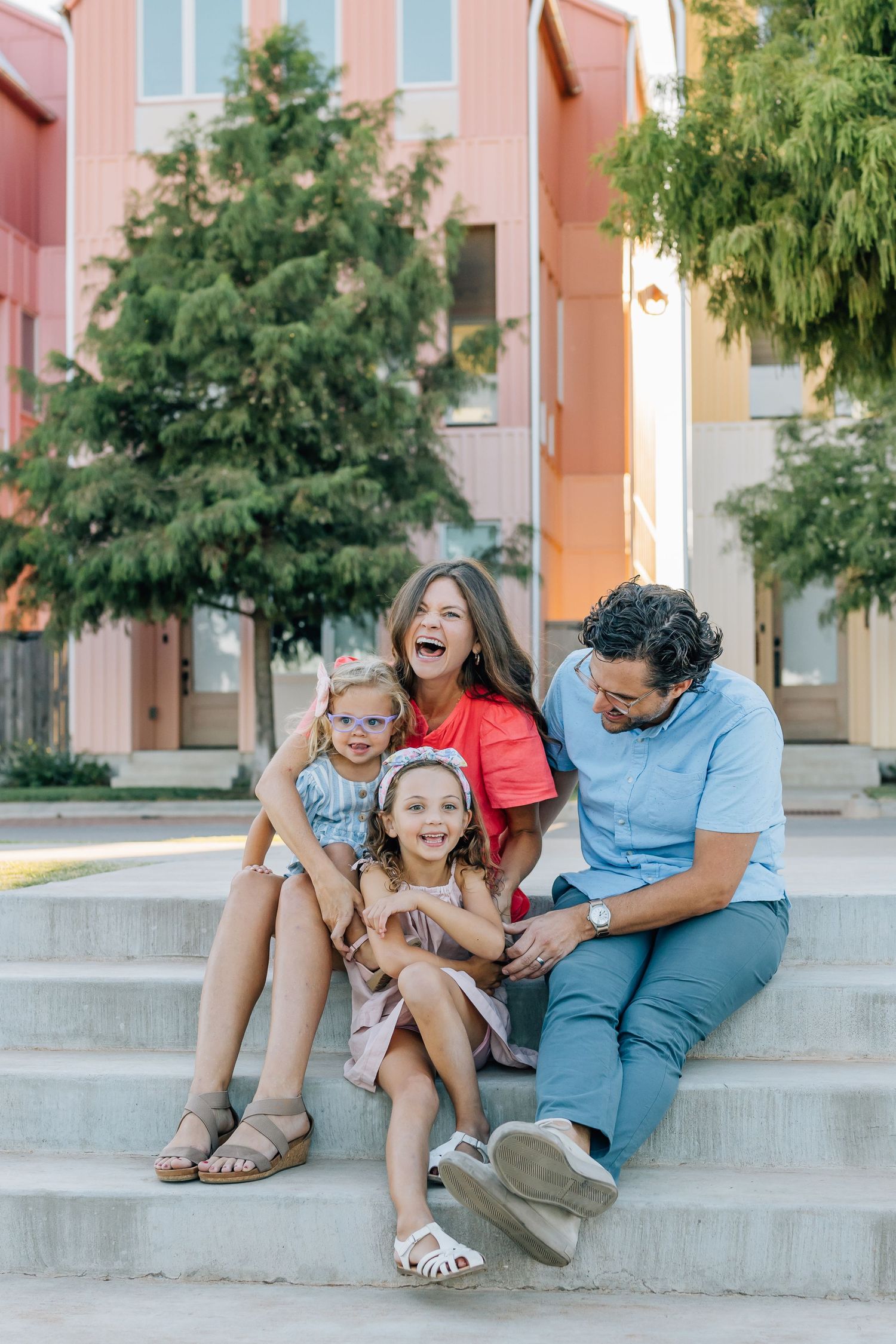 Family sits together on concrete steps sharing laughter and joyful moments during an outdoor photo session.