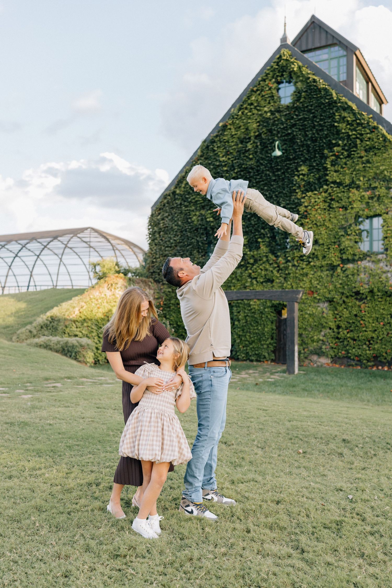 A couple dances playfully on a grassy hillside with an ivy-covered building in the background.