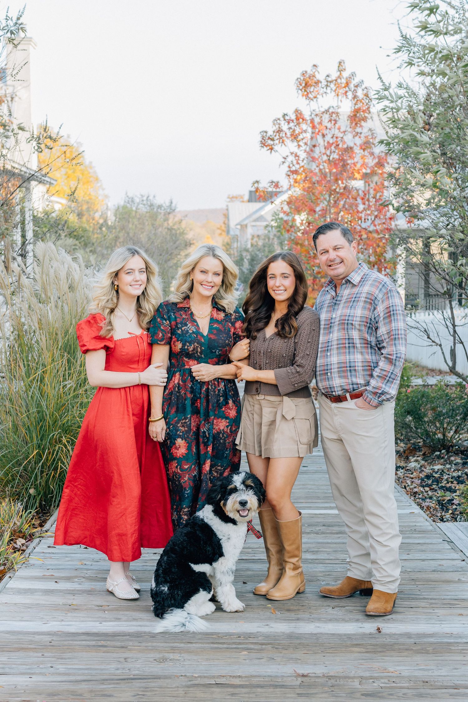 A family poses on a wooden boardwalk with their black and white dog during autumn.