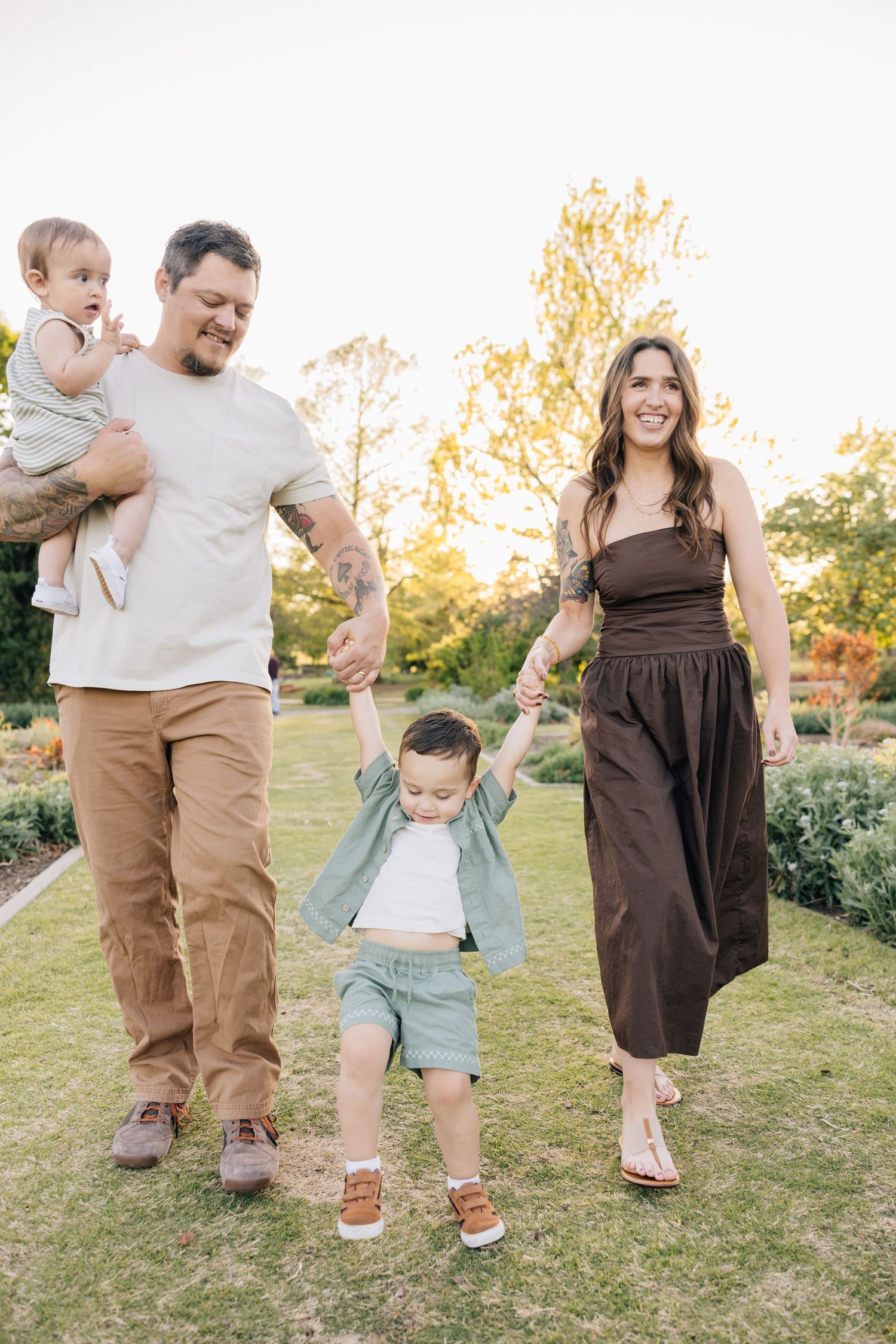 Happy family enjoying a playful moment together at sunset in a garden setting wearing casual attire.