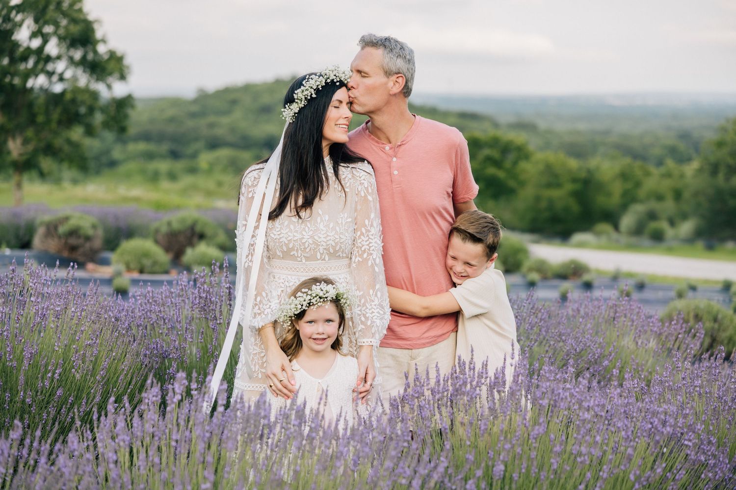 A family stands together in a beautiful blooming lavender field with rolling hills in the background on a summer day.