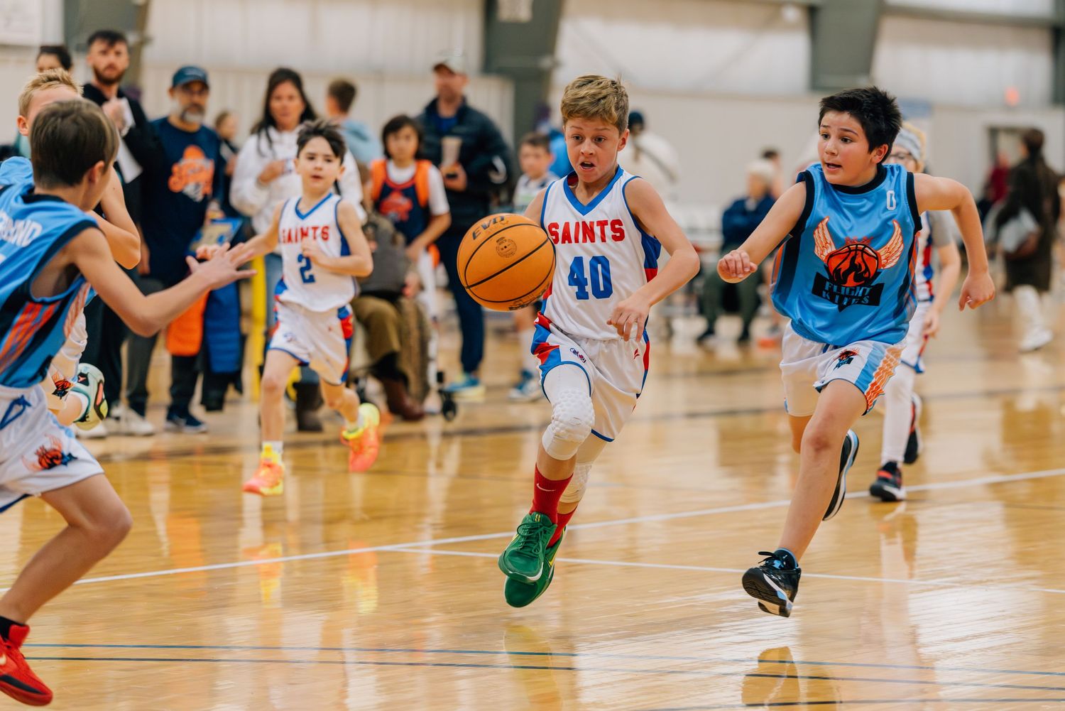 Youth basketball players compete during an intense game on a wooden court in a school gymnasium.