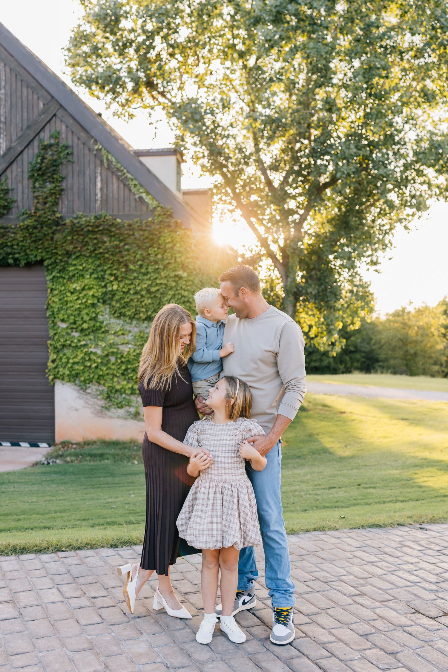 Family enjoying a sunset moment together on a stone patio with a rustic barn in the background.