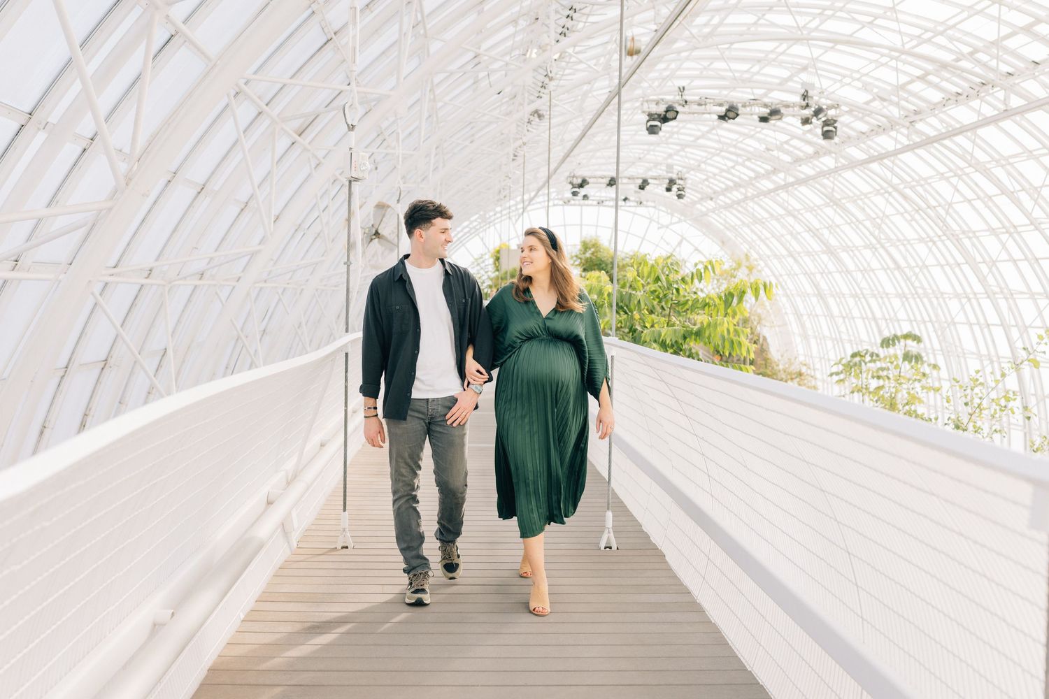 Couple walking hand in hand through a white tunnel walkway with green plants.