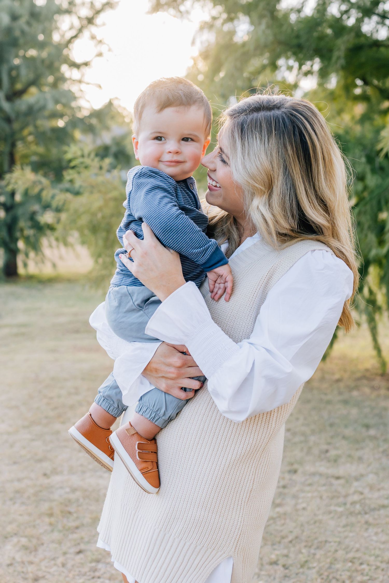 Person in white sweater holding small child outdoors in golden sunlight.