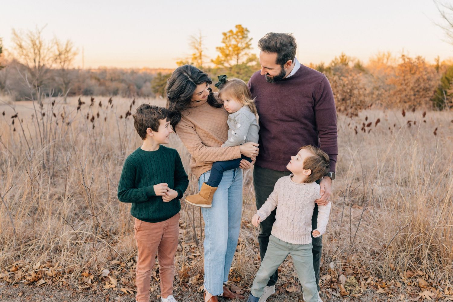 A family enjoys a tender moment together in a golden autumn field during sunset.