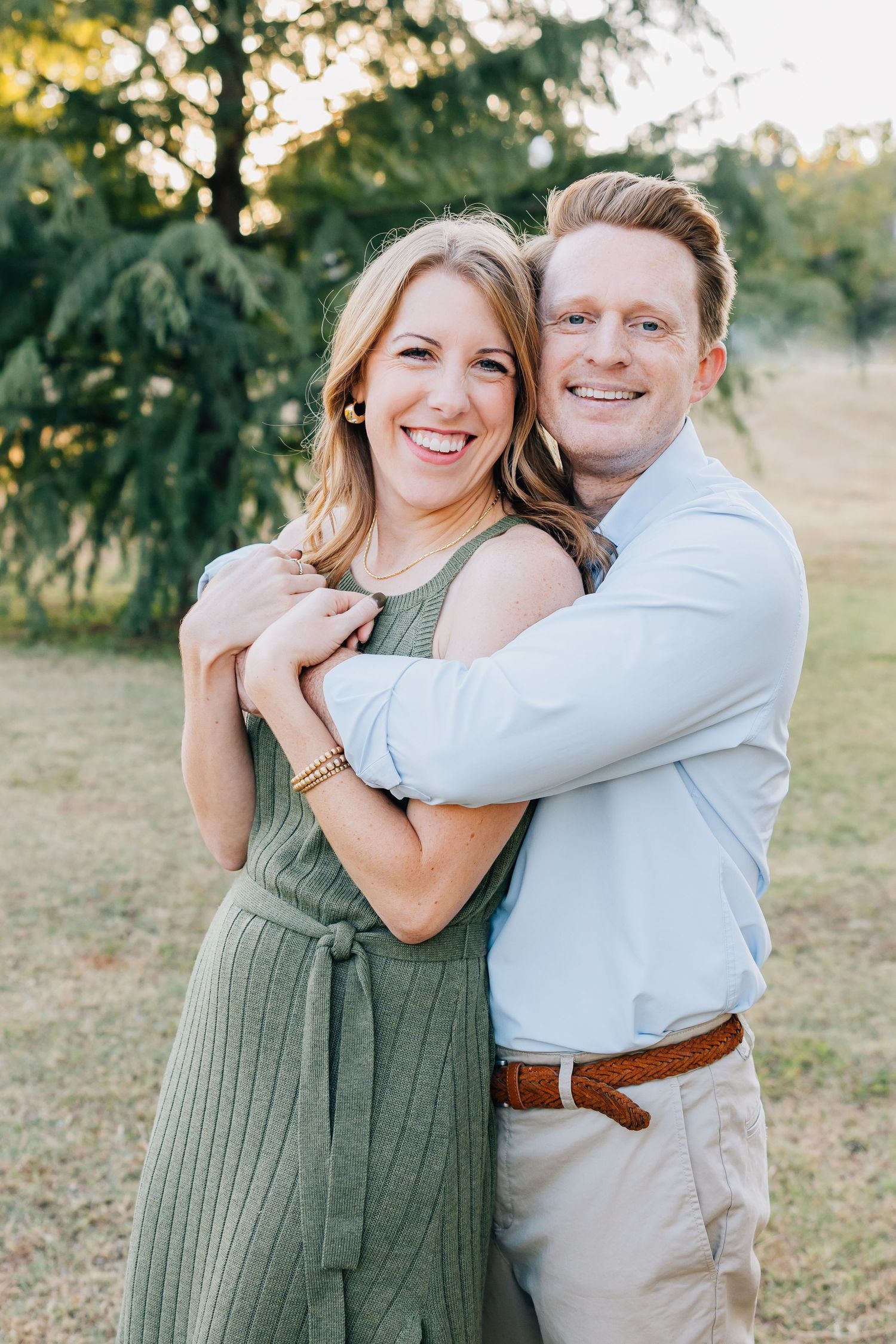 A couple embracing outdoors in casual dressy attire during golden hour.