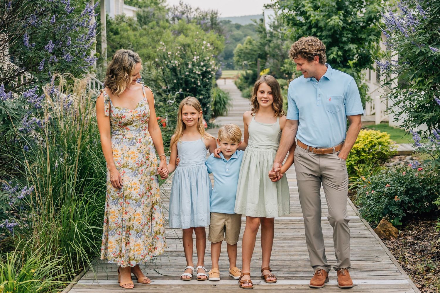 A family walks together hand in hand on a wooden boardwalk surrounded by summer gardens.
