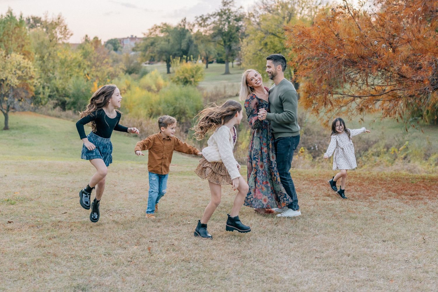 A group plays and dances together in a grassy field during autumn.