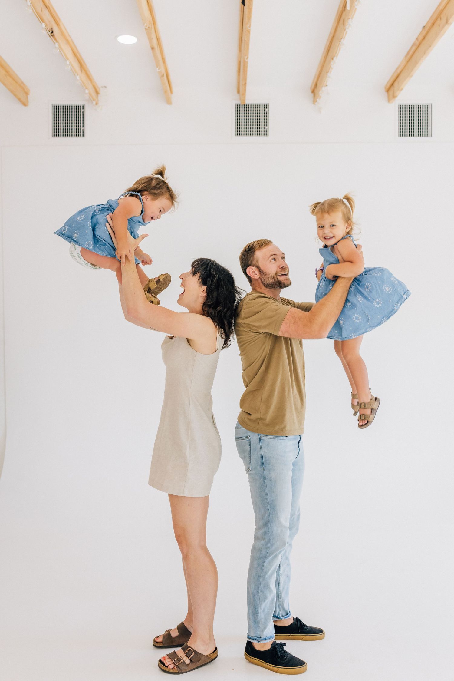 Family having fun in white studio while adults lift and play with young child in casual outfits.