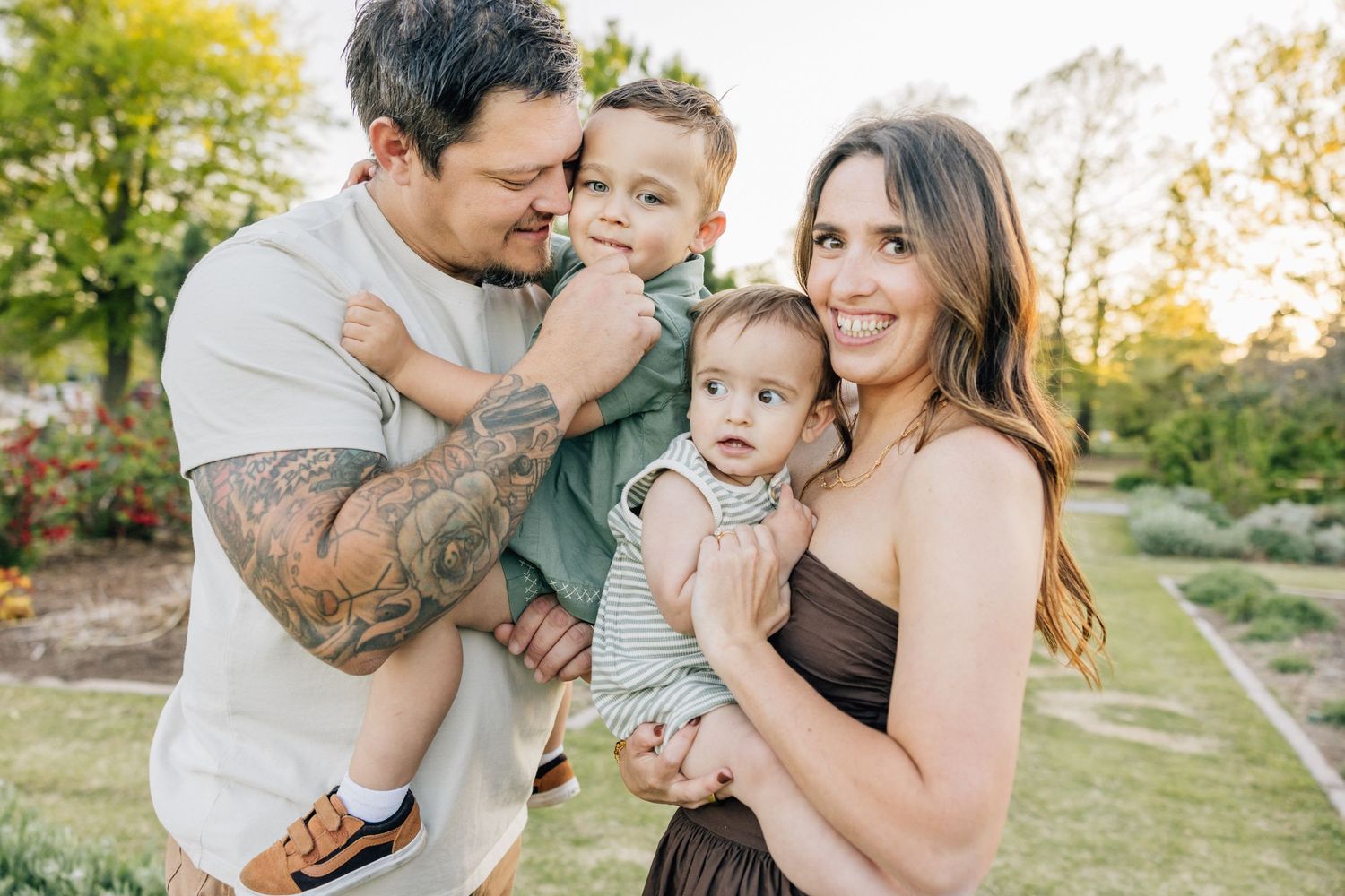 Family enjoying outdoor photoshoot in a sunlit garden on an autumn day while dressed in casual attire.