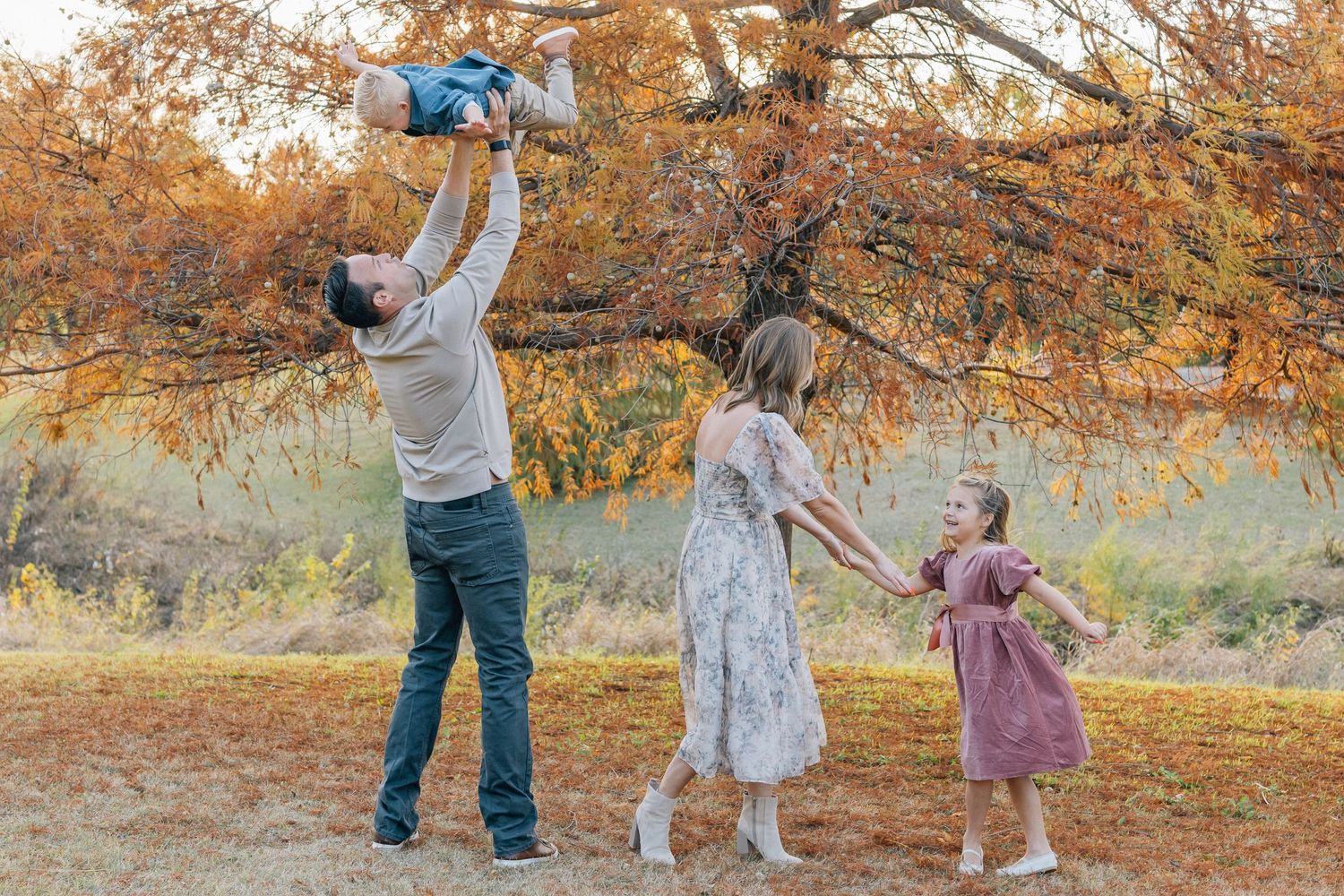Adults and children playing together in a park during autumn with orange fall foliage in the background.